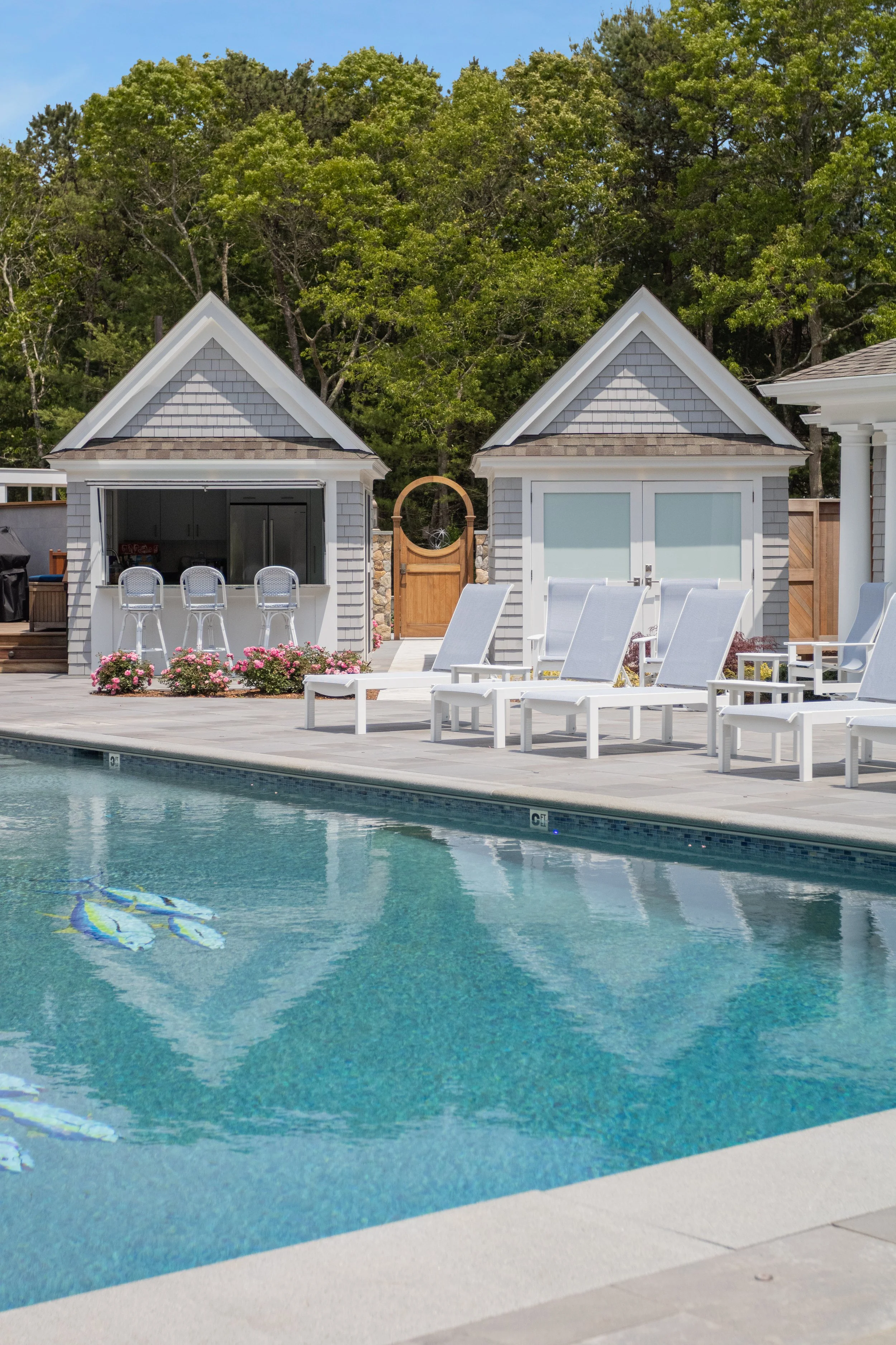 Poolside cabanas and lounge chairs beside a custom coastal home’s swimming pool terrace.