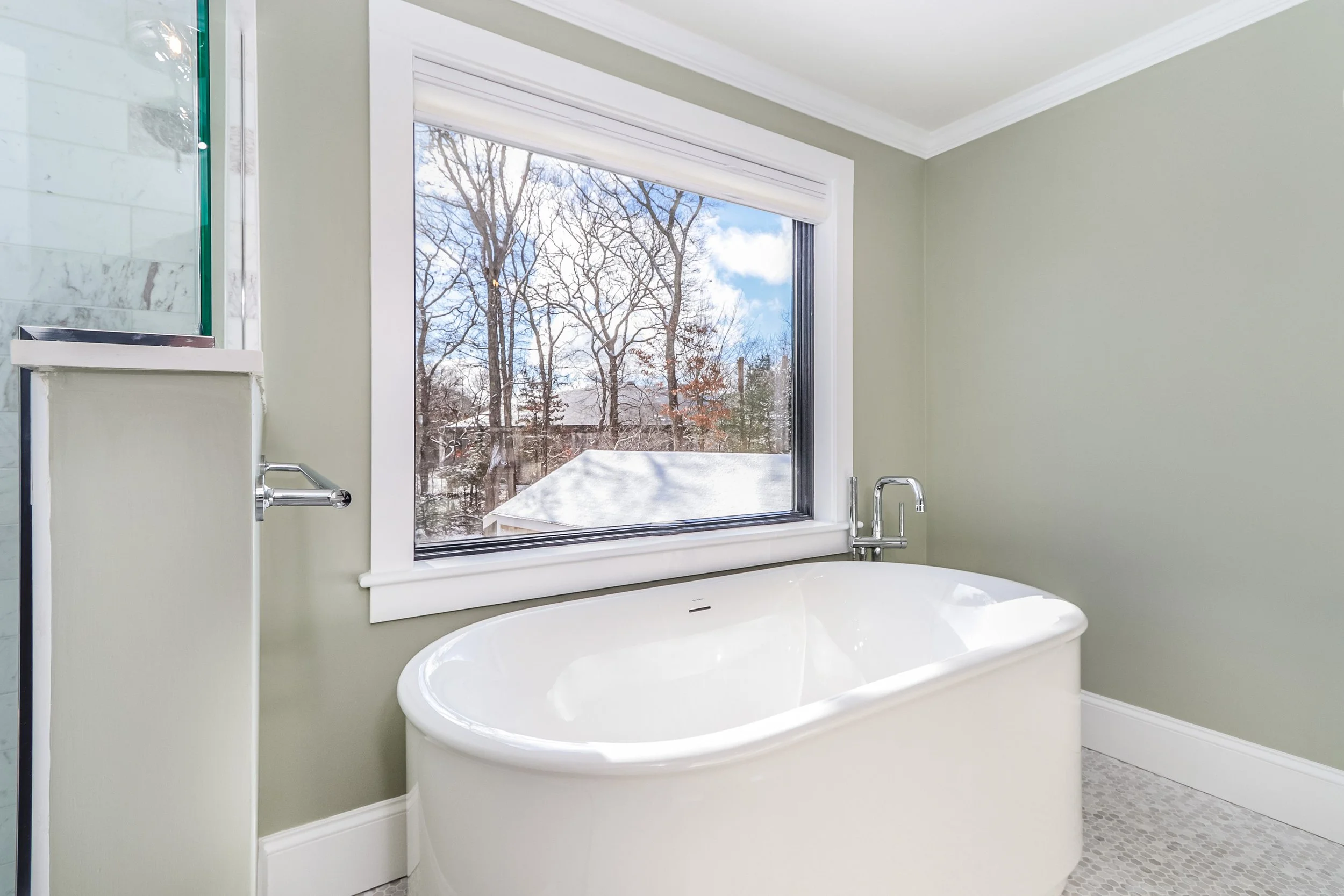This custom coastal home bath includes a freestanding tub, large window, glass shower, and mosaic tile floor.