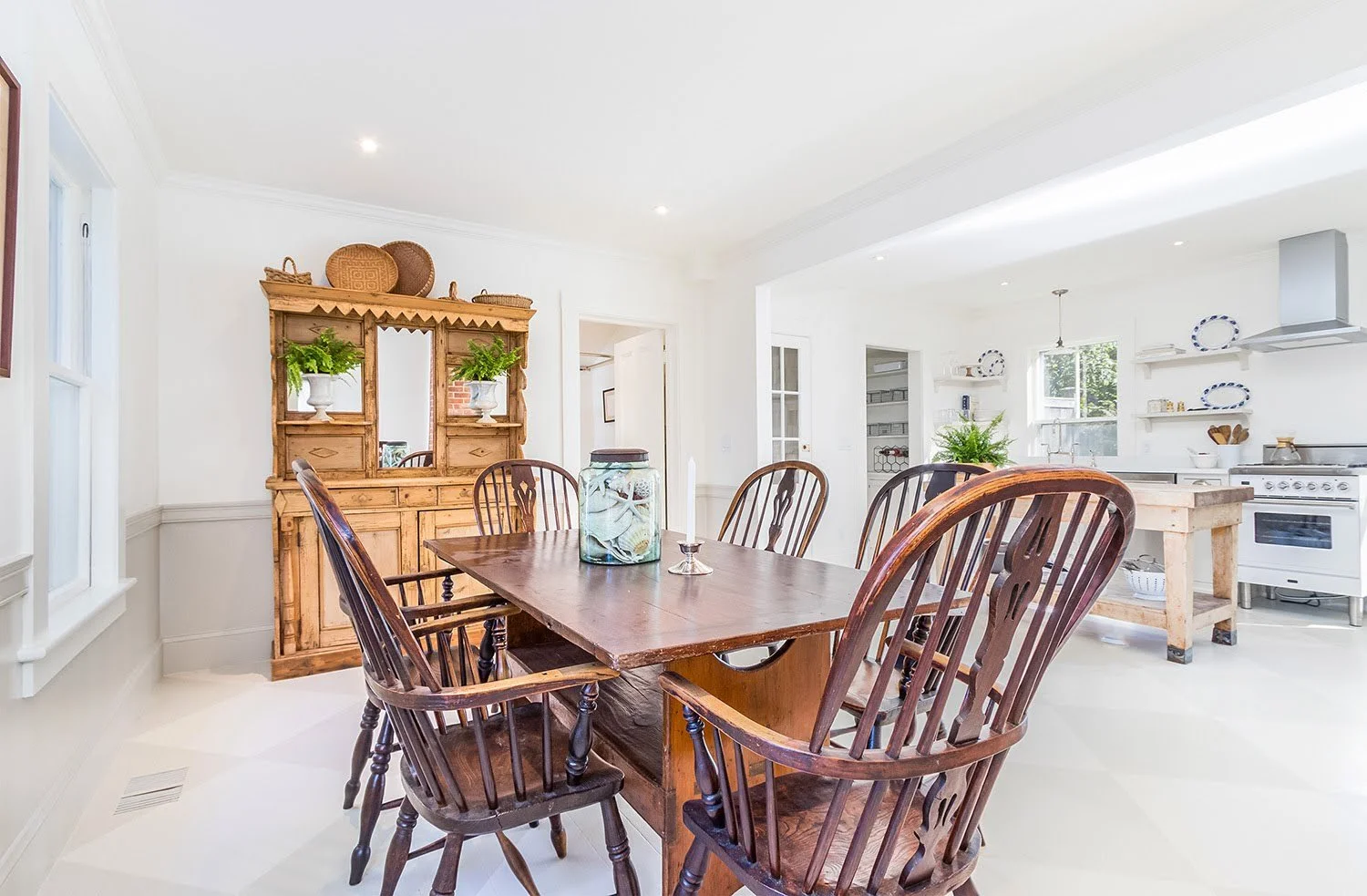 Wood dining table, antique hutch, and open kitchen create a bright Cape Cod cottage dining room.