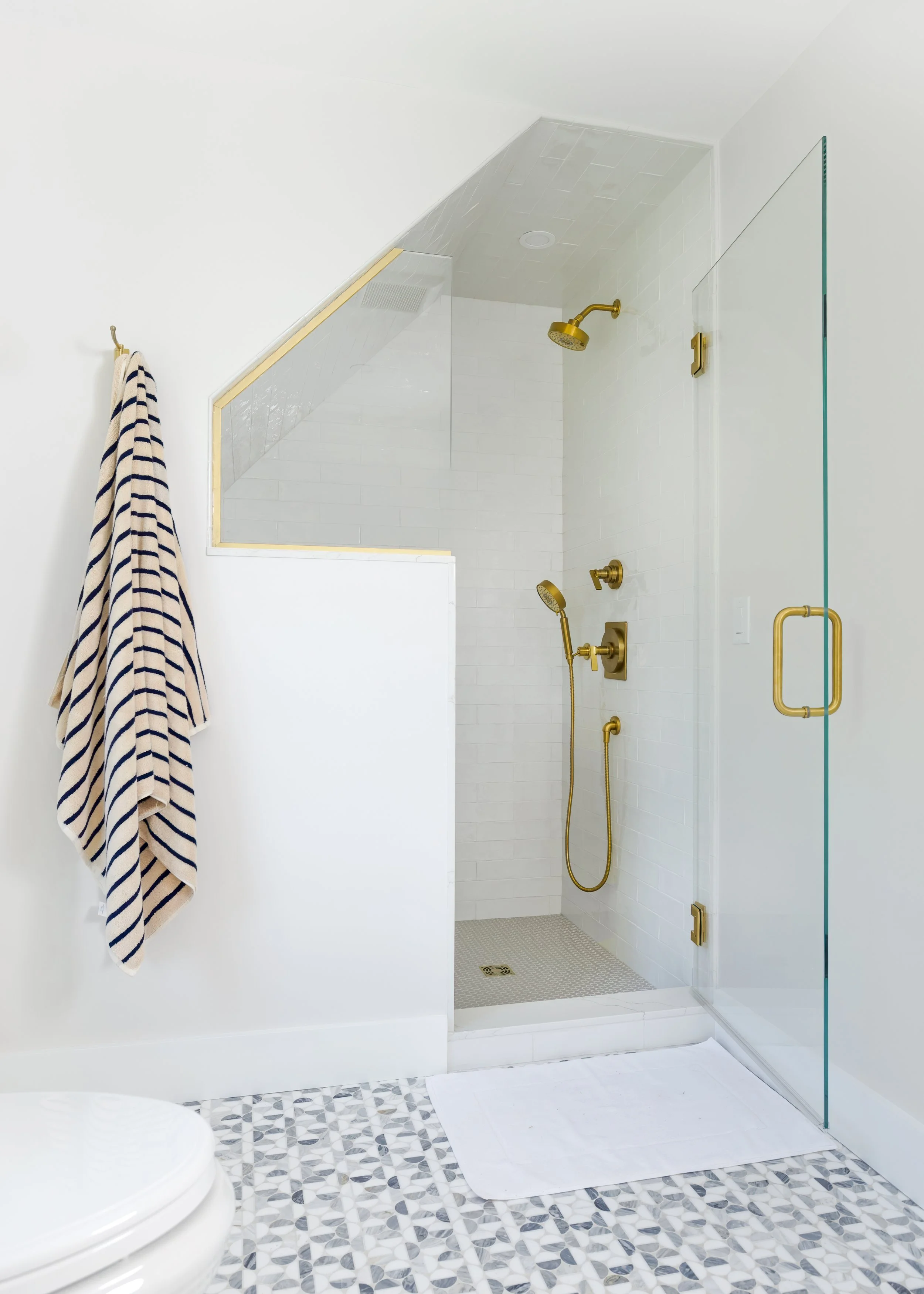 Glass shower with gold fixtures and patterned floor tile gives this coastal bath renovation a crisp finish.