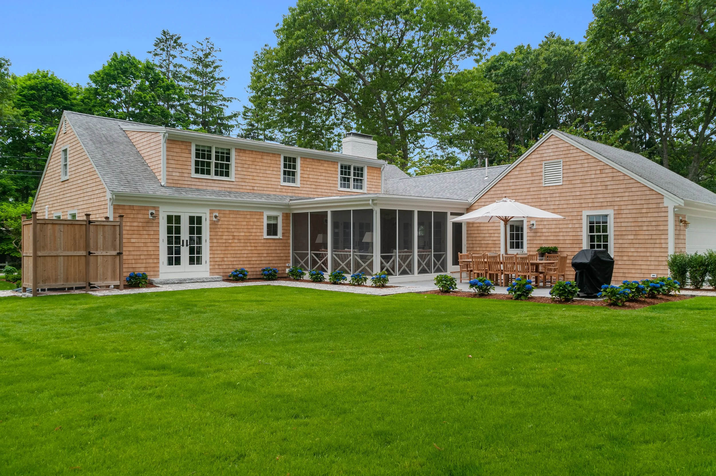 Shingled Cape Cod home with screened porch, outdoor dining area, green lawn, and custom coastal detailing.