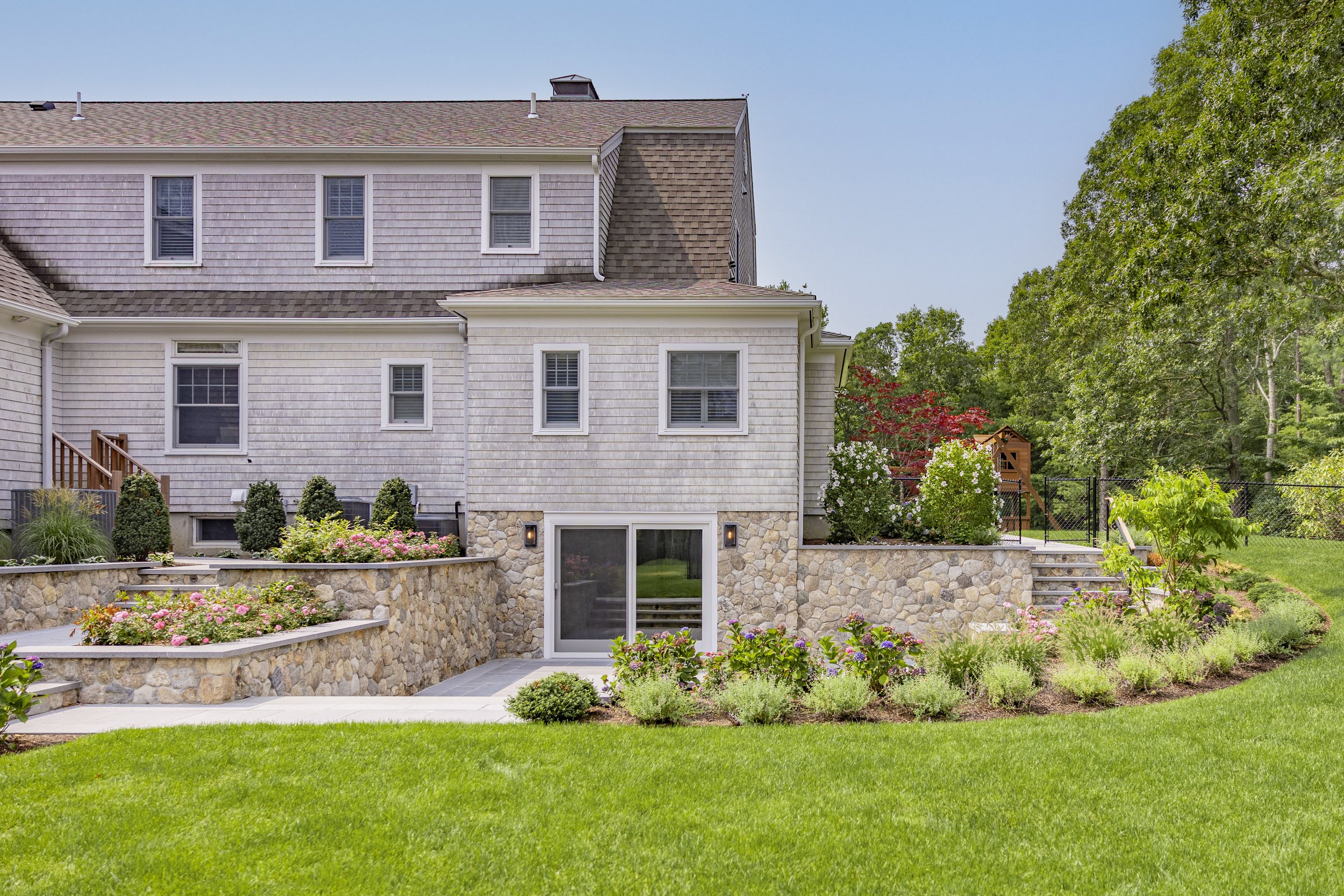 Cape Cod home exterior with stone garden walls, flowering landscaping, and manicured lawn.