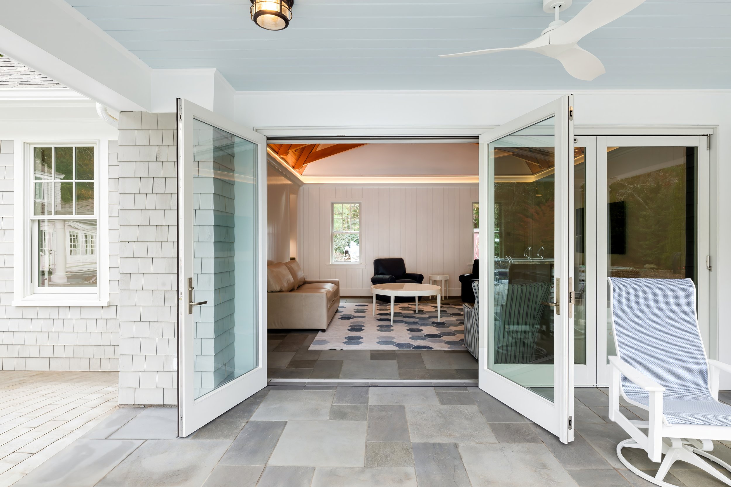 Open glass doors connect a covered patio to a bright living area in a custom coastal home.