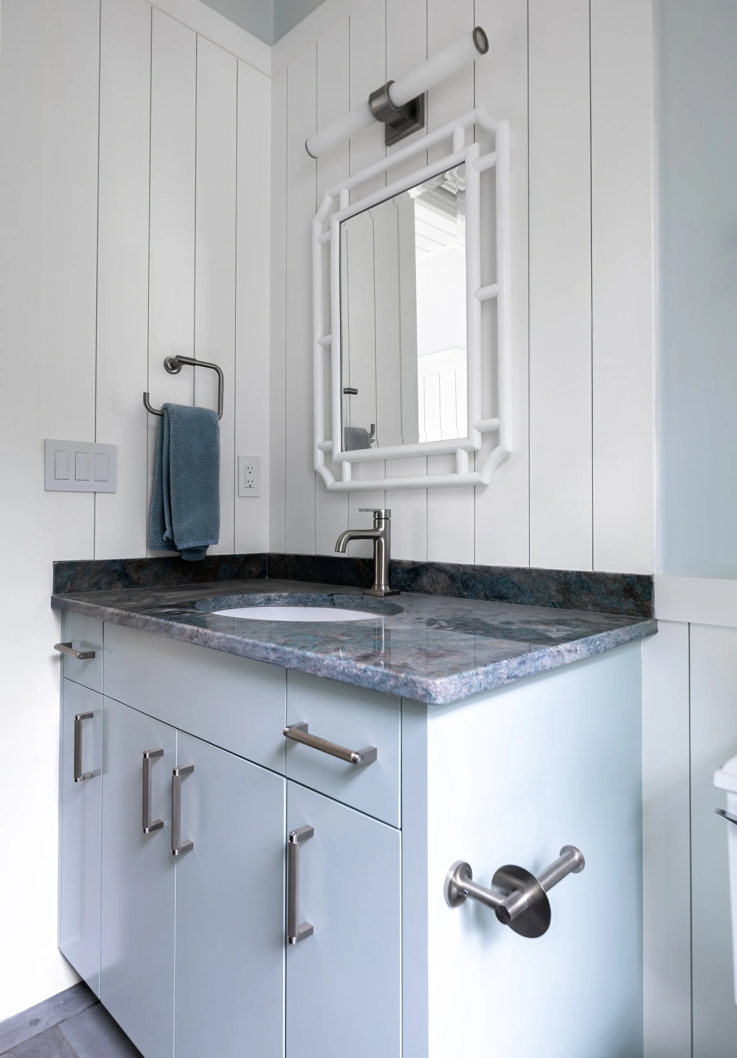 Cape Cod pool house bathroom vanity with stone countertop, white paneling and polished nickel hardware/