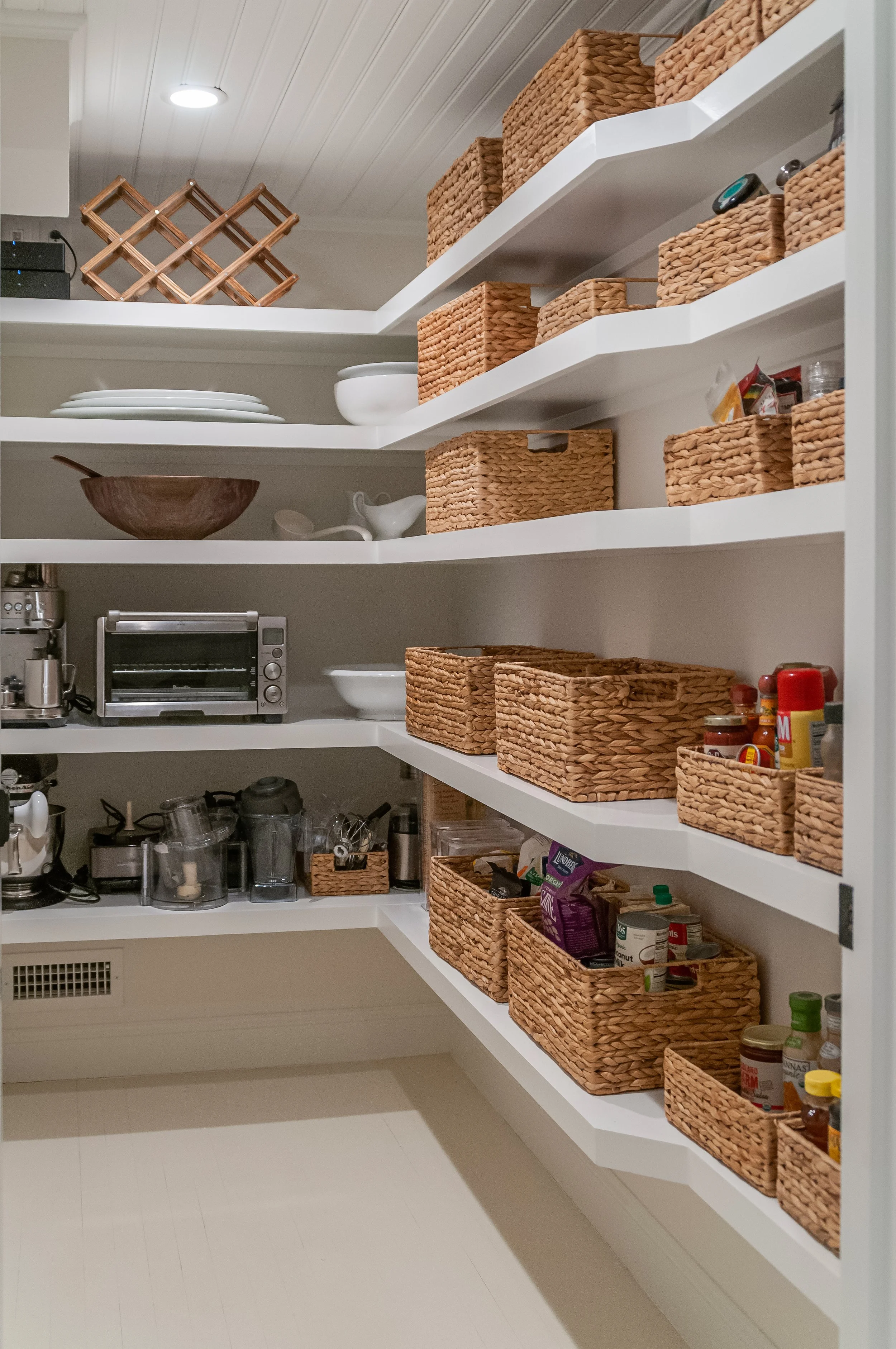 Walk-in pantry in a custom Cape Cod home with open shelving, woven storage, and organized kitchen essentials.