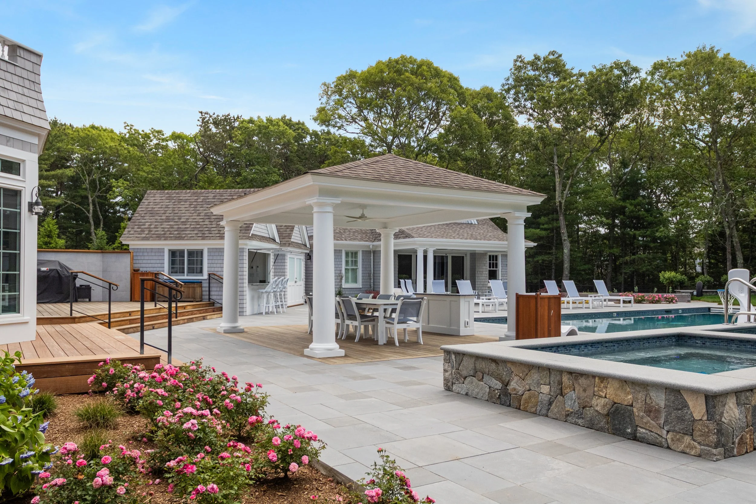 Covered poolside dining pavilion with stone spa, lounge chairs, and gardens at a custom coastal home.