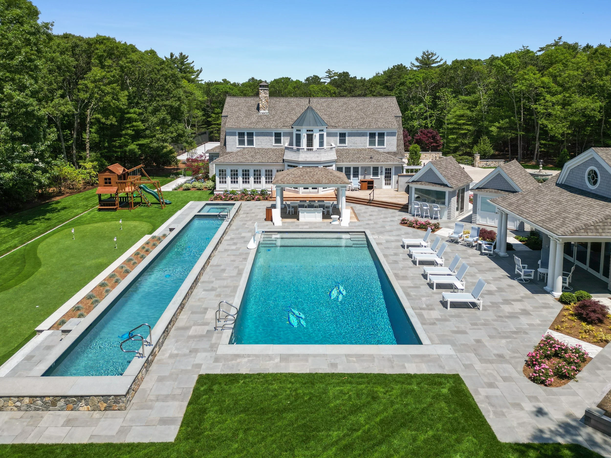 Aerial view of a custom coastal home with pool terrace, cabanas, and manicured lawn.