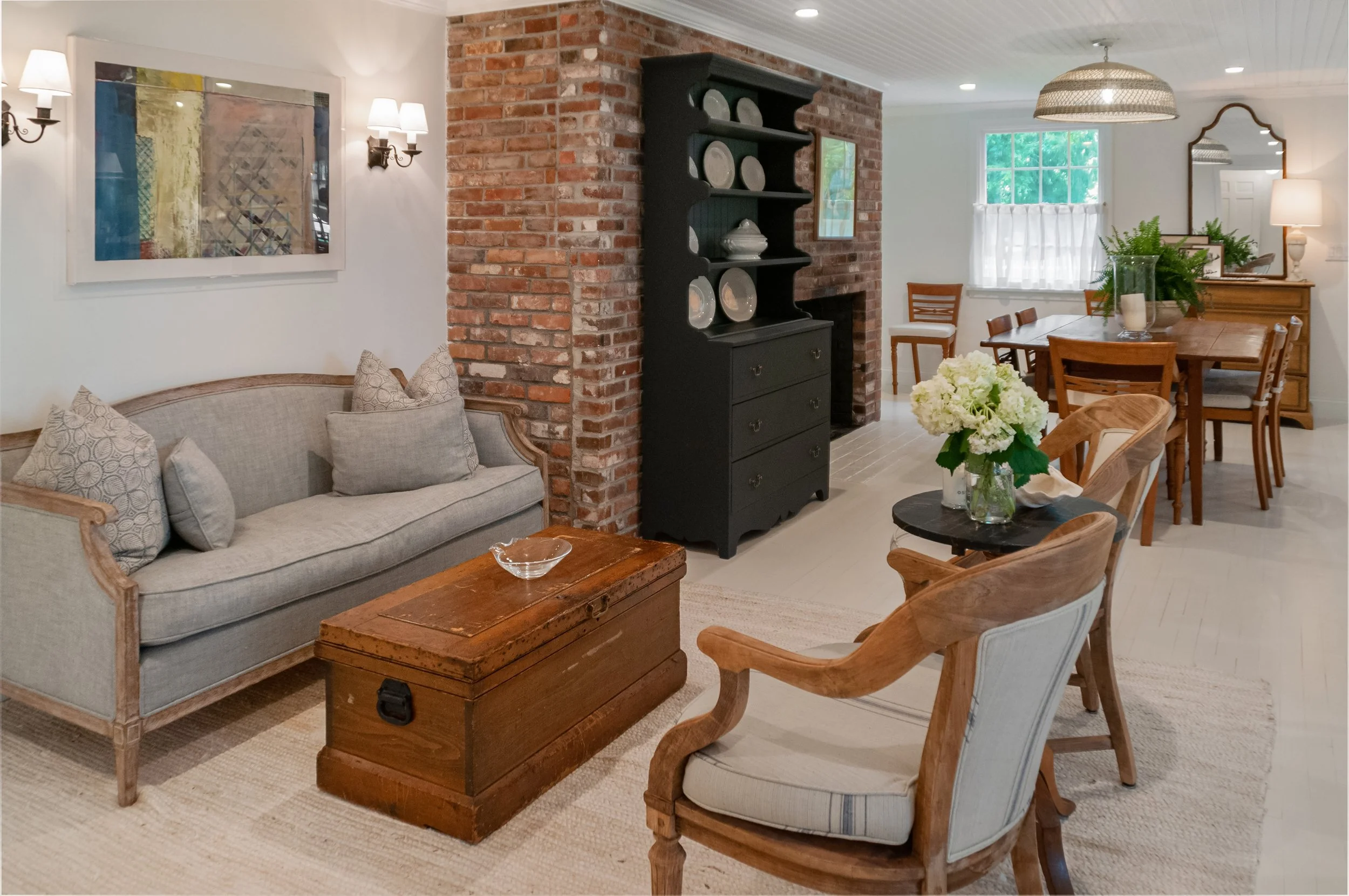 Sitting and dining room with brick fireplace wall, built-in shelving, and custom coastal home furnishings.
