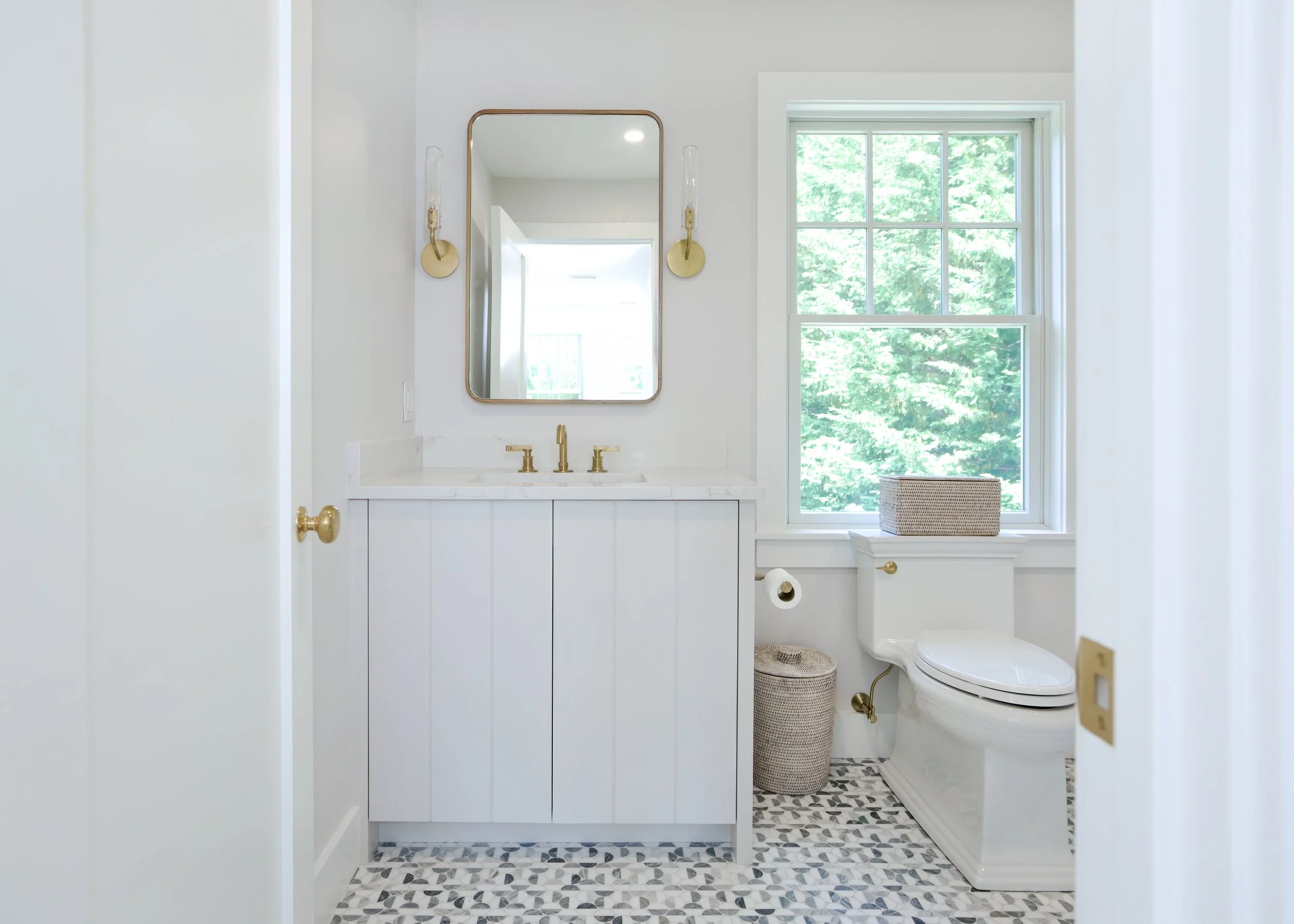 Brass fixtures, patterned tile, and a paneled vanity bring fresh coastal bathroom design to this space.