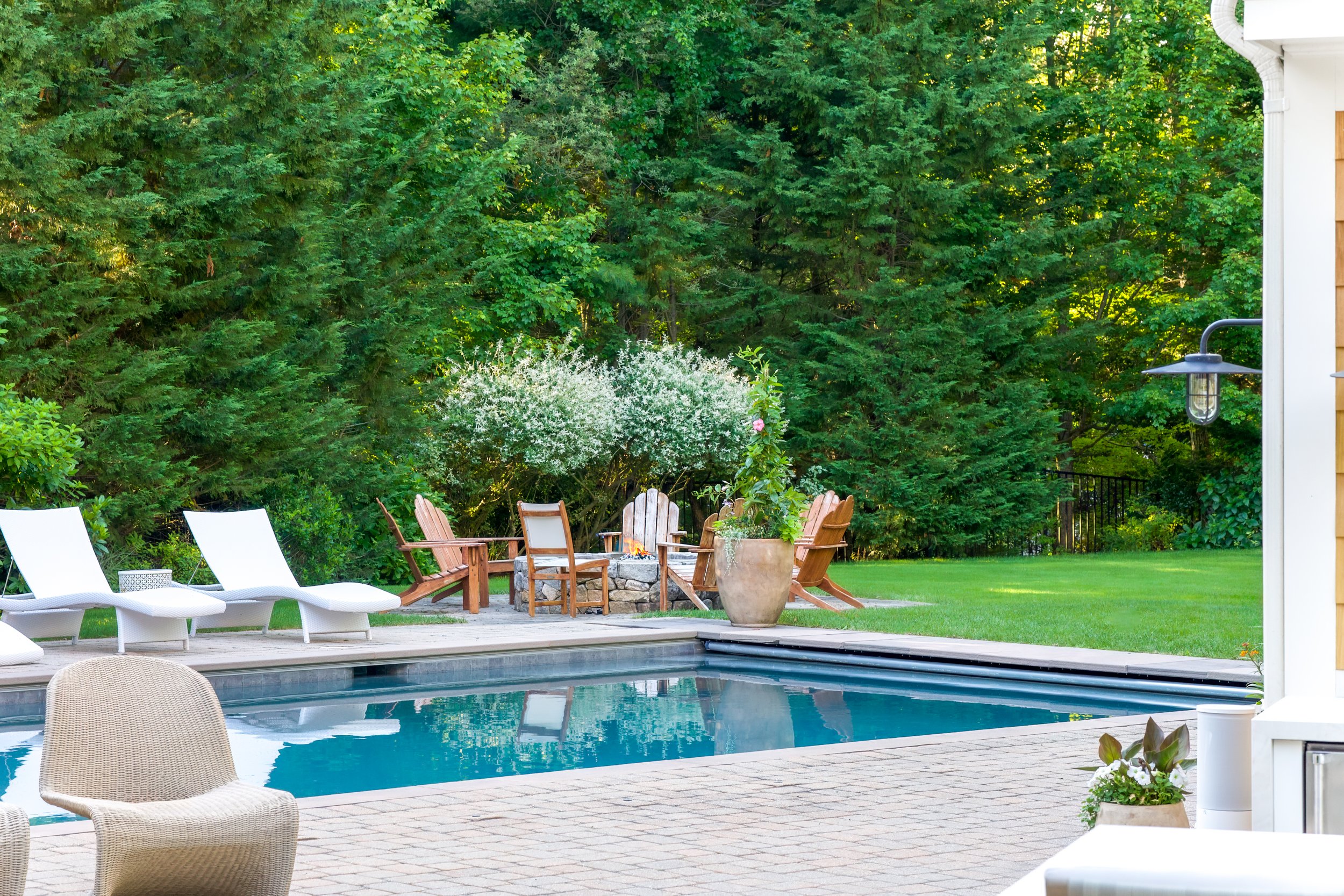 Lounge chairs, pool , and wooded seating create a serene Cape Cod backyard retreat.
