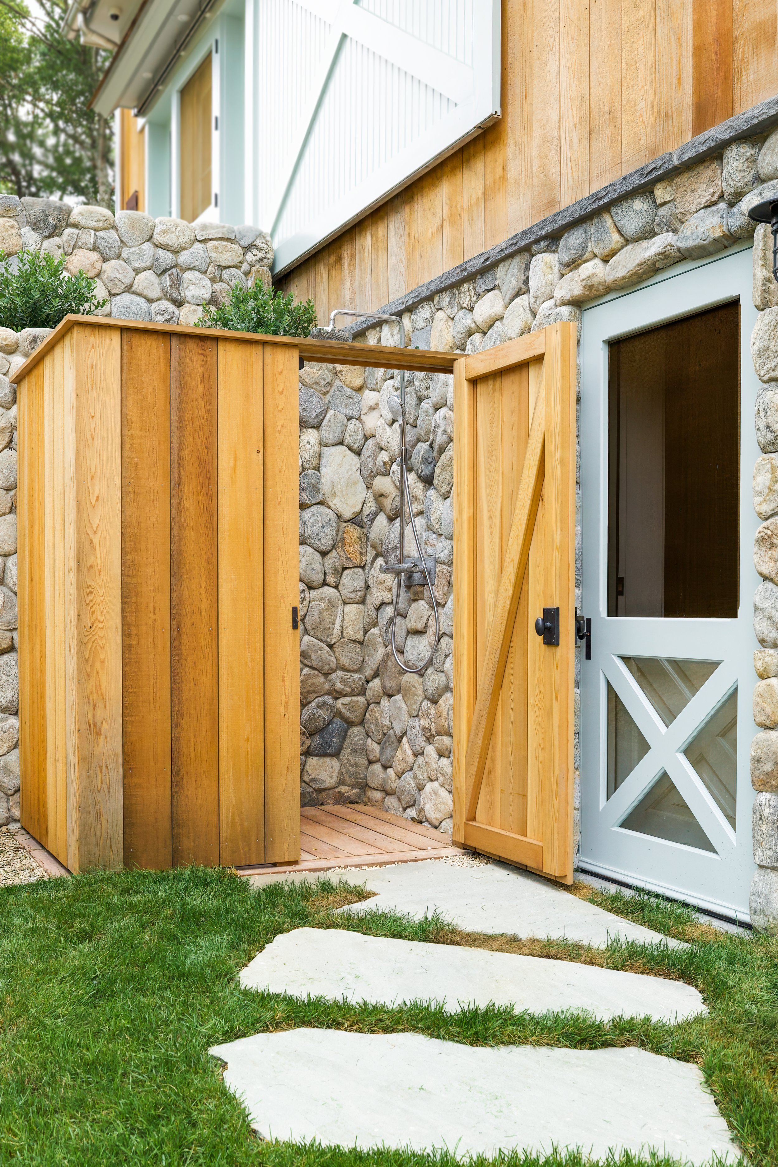 Built into a fieldstone wall, this Sea View Builders outdoor shower features custom cedar privacy panels, a private changing area, and timeless Cape Cod outdoor living.