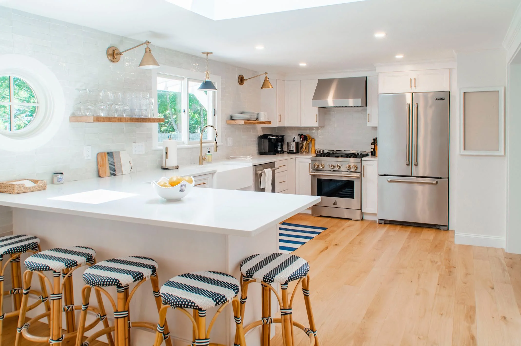 Sunlit custom coastal home kitchen features island seating, brass accents, stainless appliances, and bright Cape Cod style.