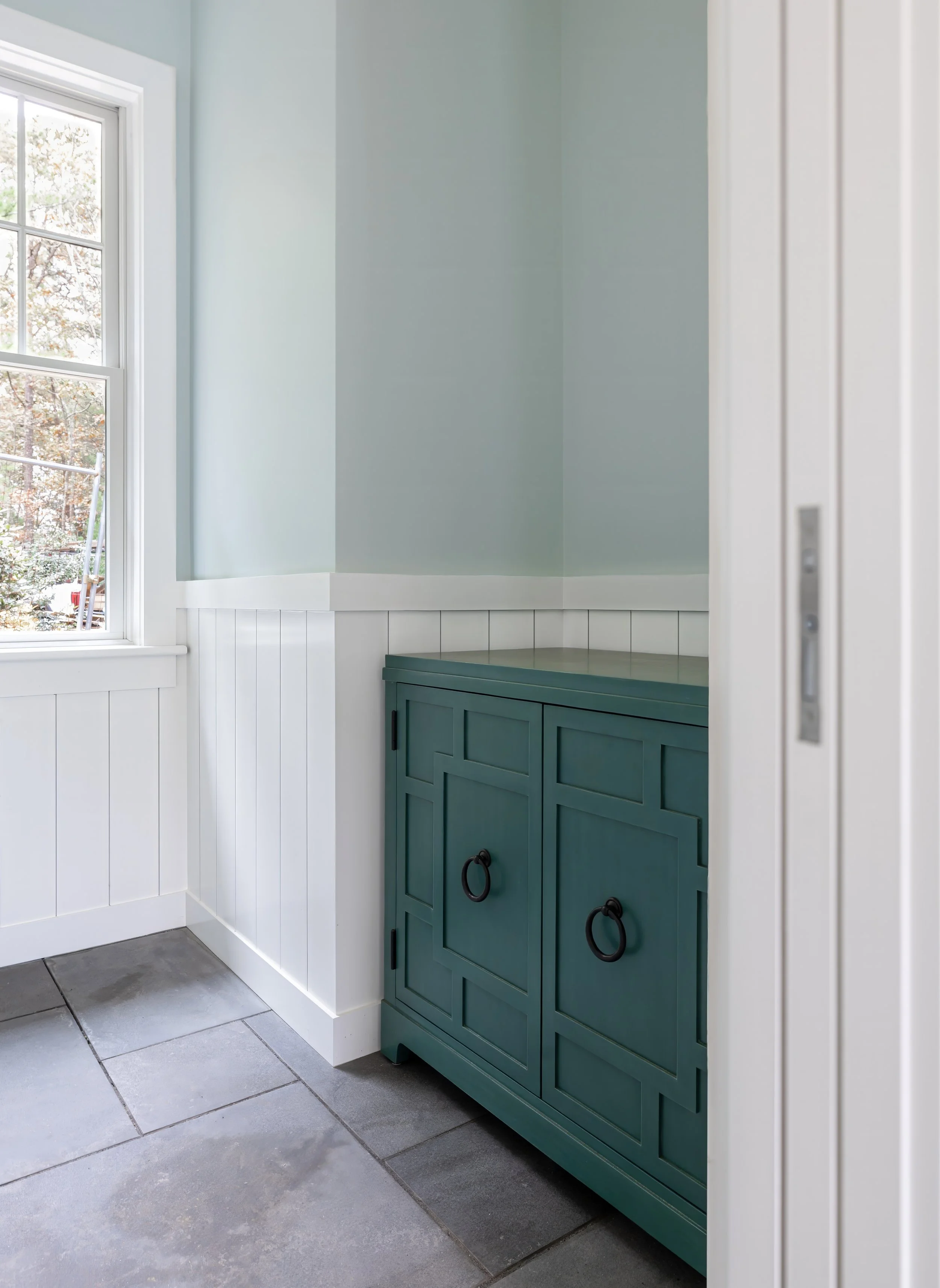 Pool house nook with teal cabinet, white wainscoting, slate flooring, and natural lighting