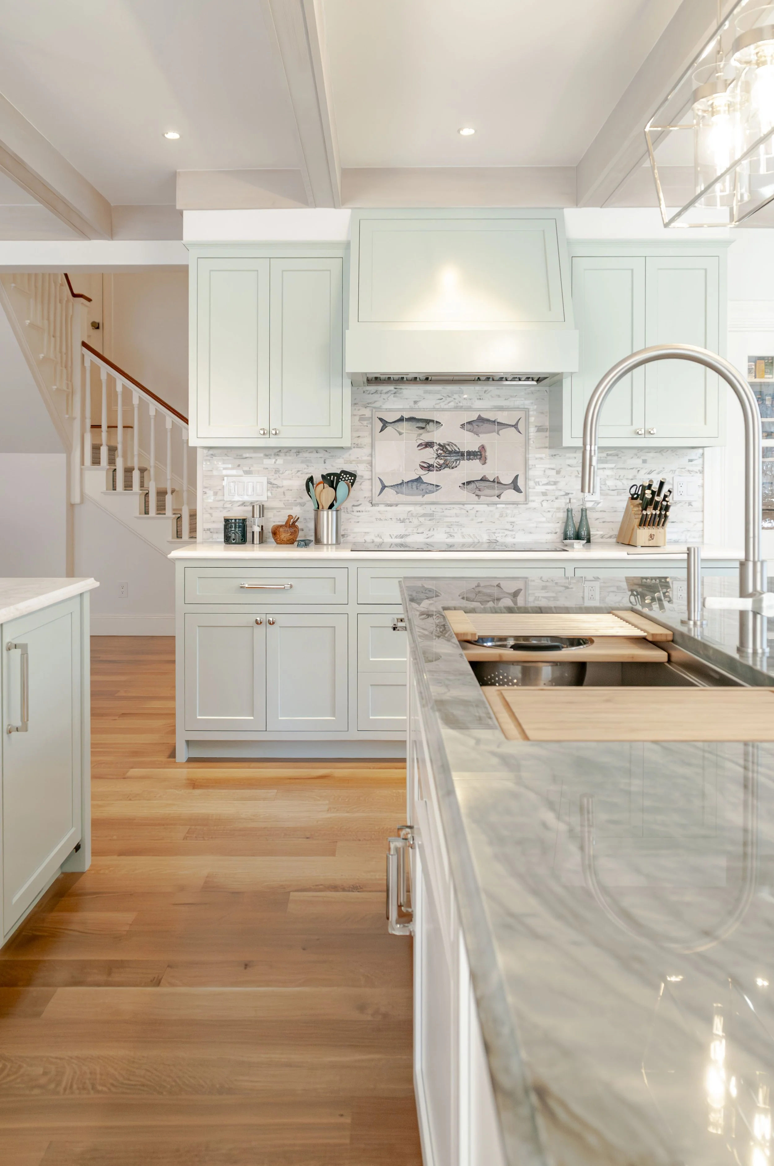 Cape Cod kitchen with marble island, pale cabinetry, fish tile backsplash, and warm wood flooring.