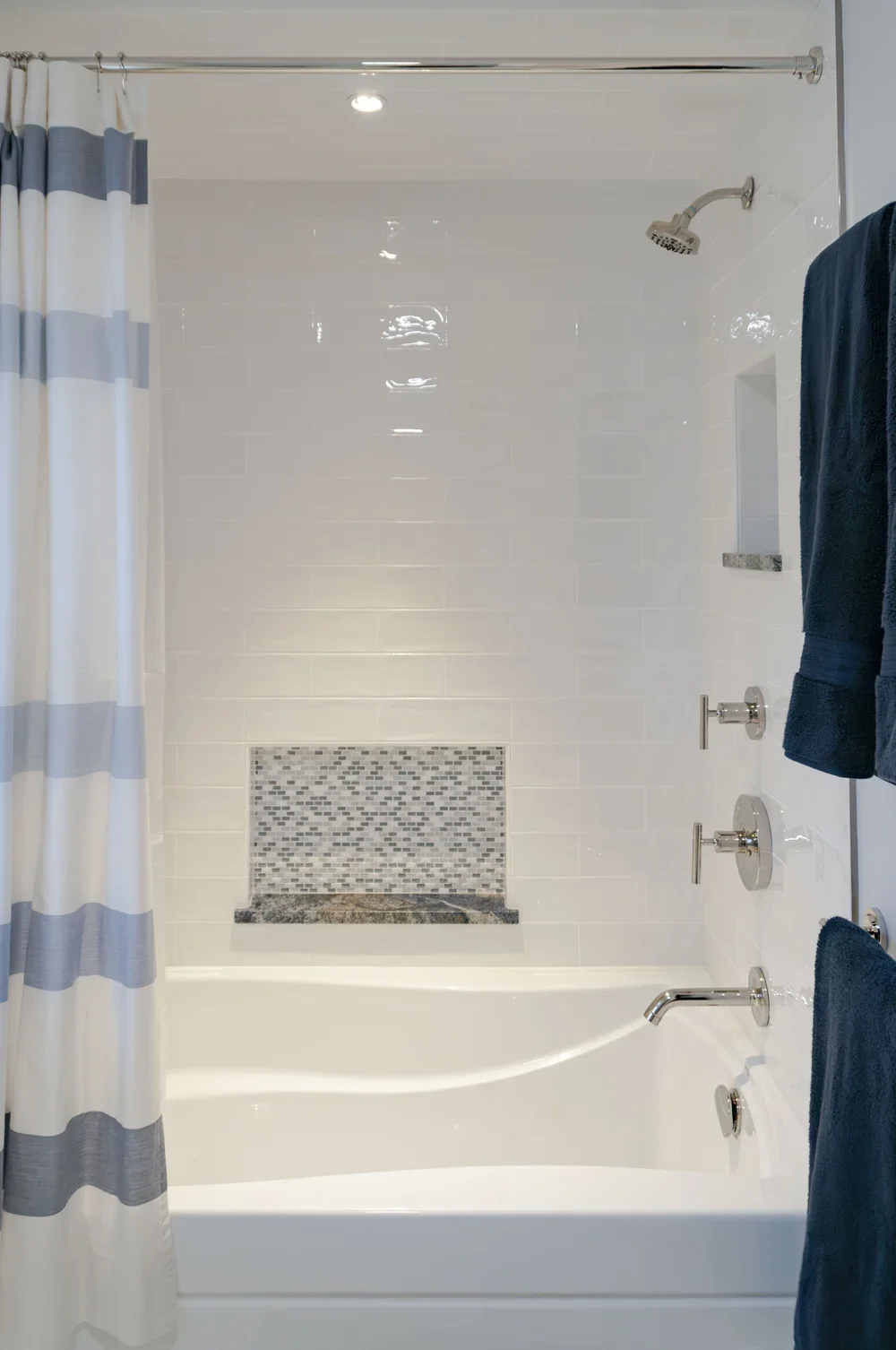 White tile and mosaic niche bring custom coastal home detail to this bright tub shower.