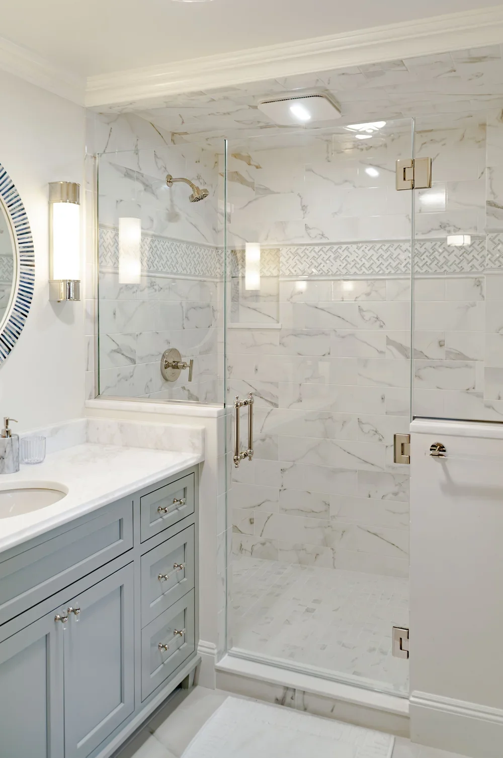 Marble-look shower tile and soft blue cabinetry bring luxury home builder in Osterville detail to this bath.