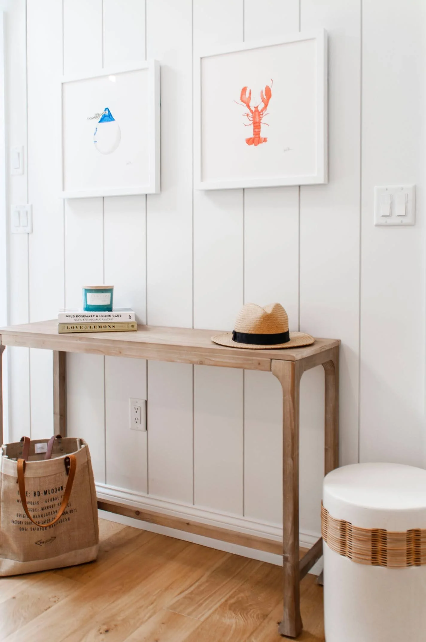 Coastal entry detail with vertical paneled walls, framed nautical artwork, wood console table, and warm oak floors.