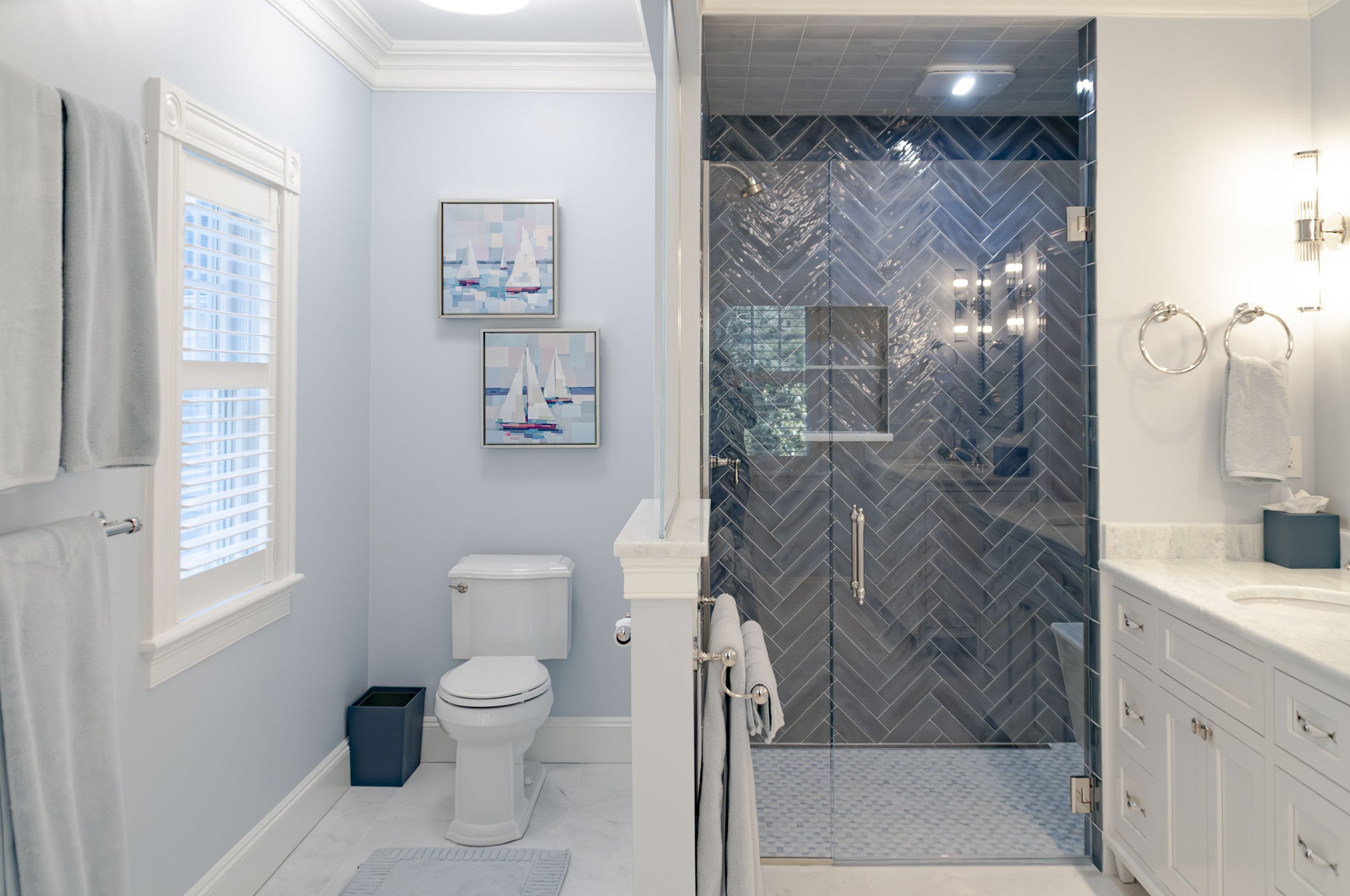 Cape Cod bathroom with glass shower, blue tile, white vanity, marble counters, and soft blue walls.