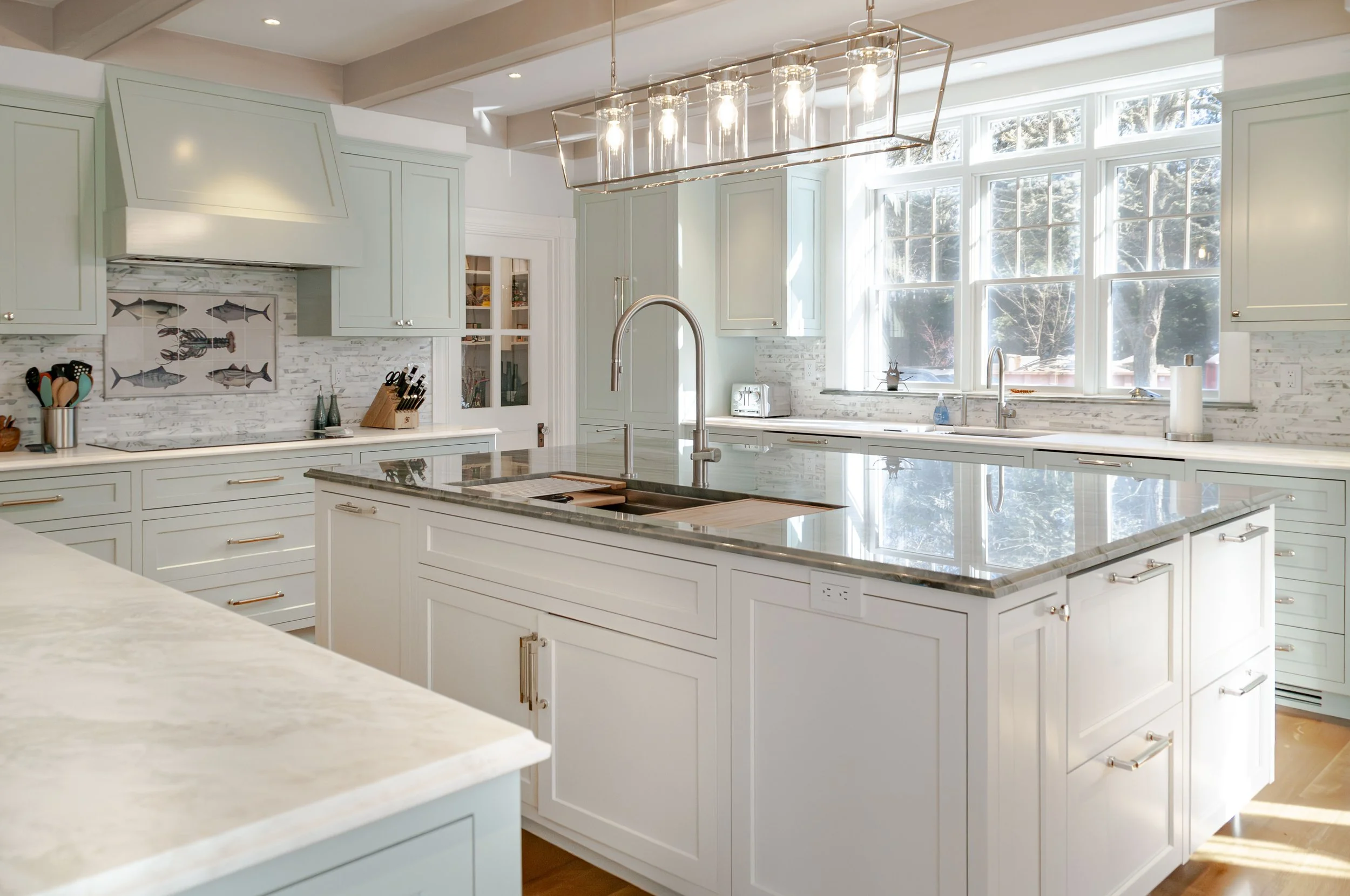 Anchored by a spacious island, this Sea View Builders kitchen features custom cabinetry, quartz countertops, designer lighting, and timeless Cape Cod coastal design.
