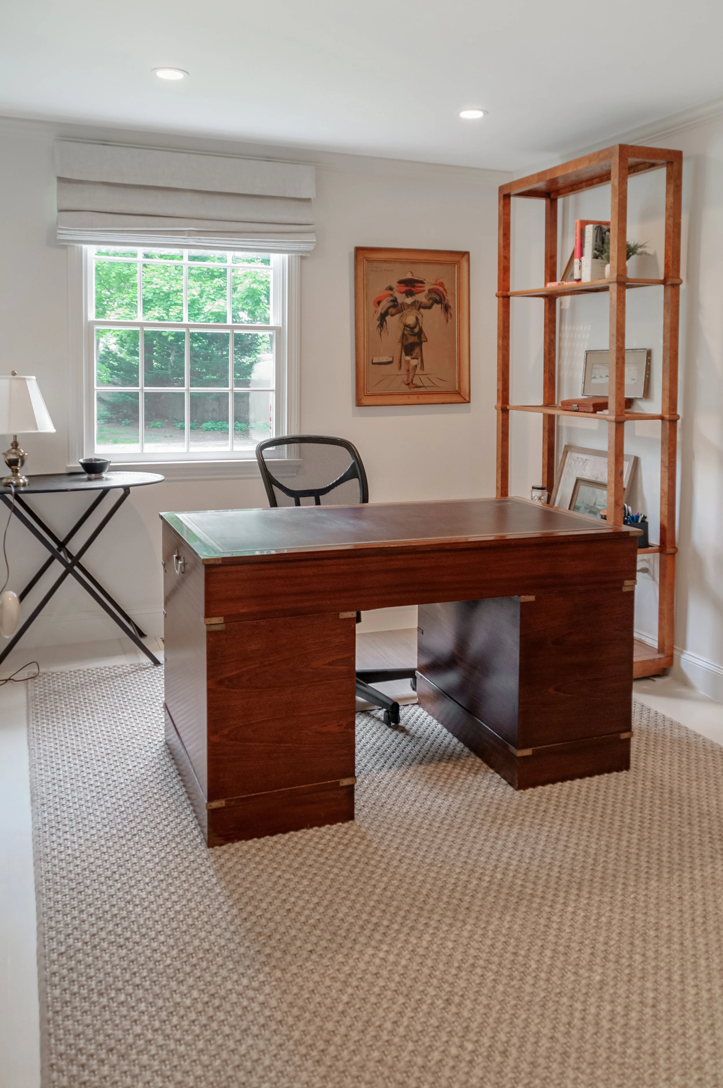 Home office in a Cape Cod interior renovation with wood desk, window view, open shelving, and framed art.