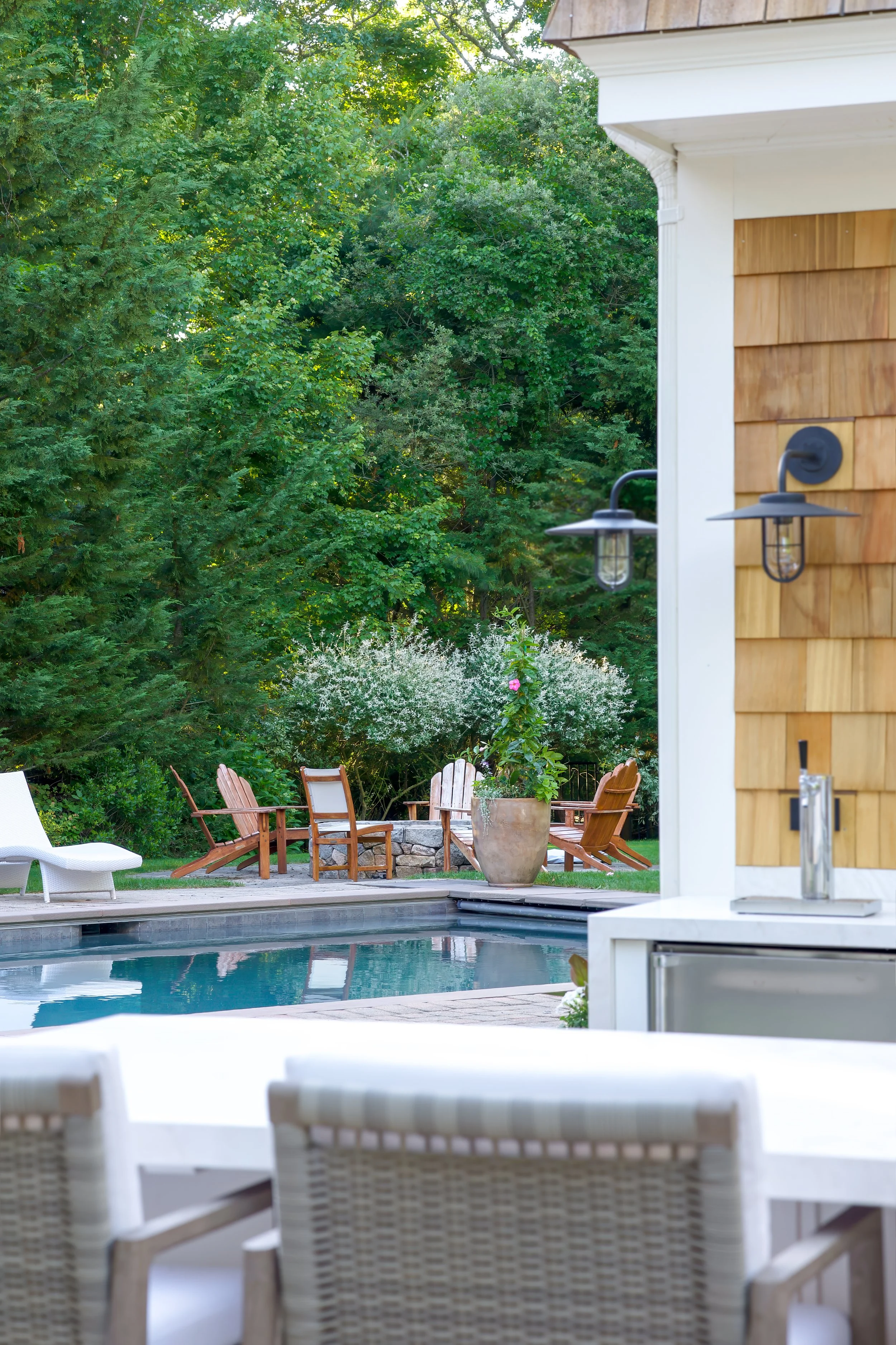 Poolside seating, wooded views, and shingled siding frame this Cape Cod outdoor living area.