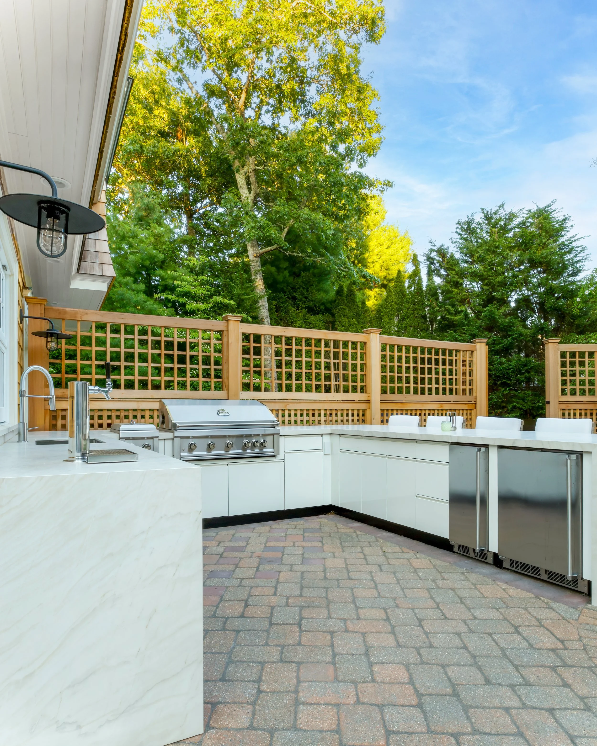 Luxury outdoor living area with a custom outdoor kitchen, natural stone countertops, built-in barbecue, paver patio, and Cape Cod backyard entertaining design.