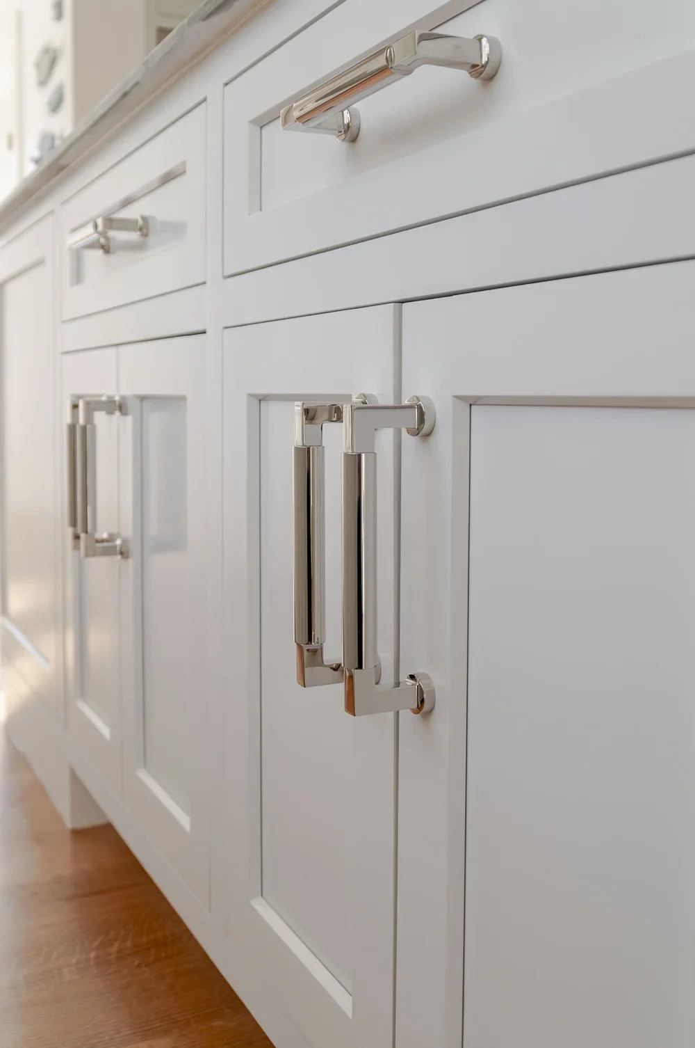 Polished cabinet hardware and pale millwork bring refined detail to this high-end Cape Cod renovation kitchen.