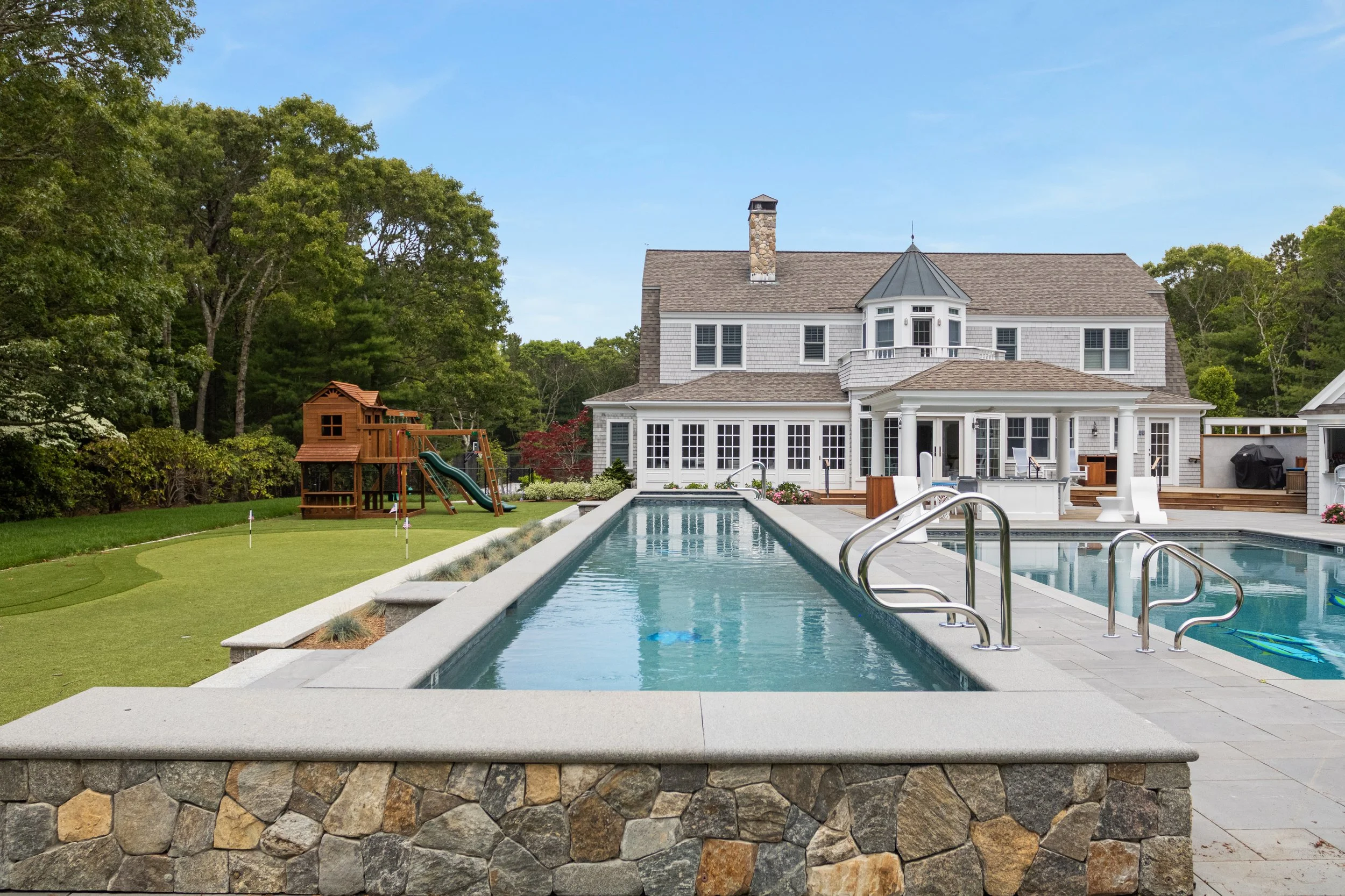 Custom coastal home with lap pool, pool terrace, putting green, and backyard playset.