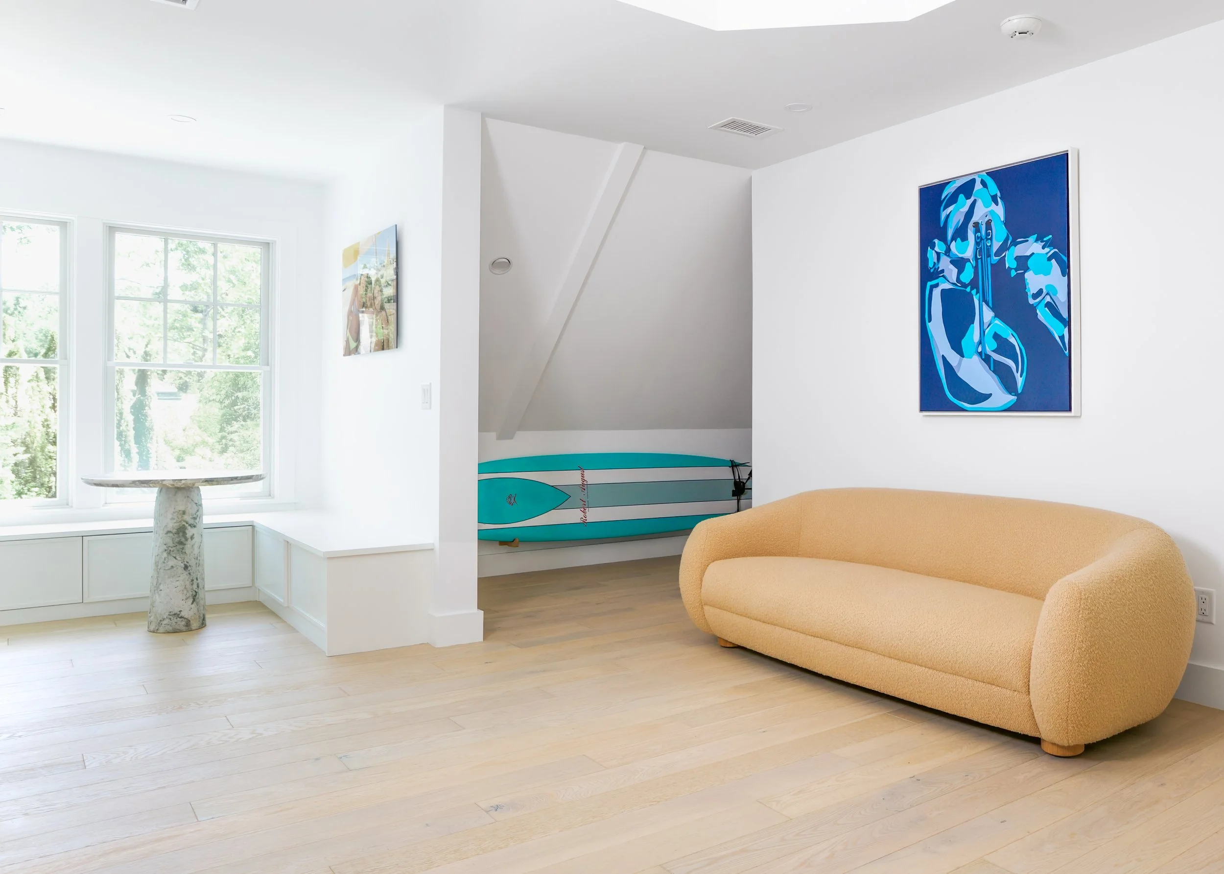 Bright pool house lounge with curved sofa, paddle board, artwork, and Cape Cod interiors style.
