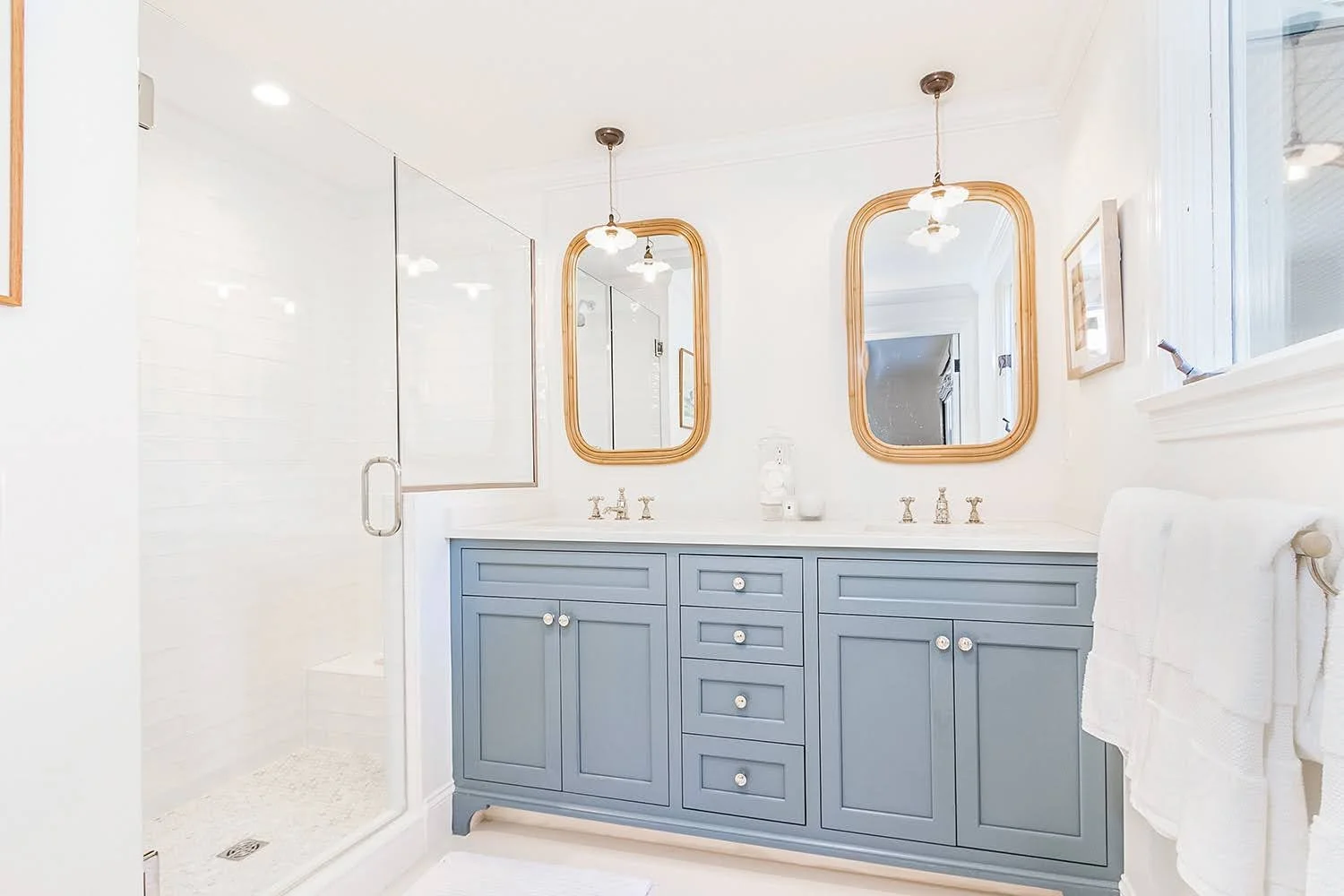 Dual gold-framed mirrors and a blue double vanity add custom coastal home detail to this bright bath.
