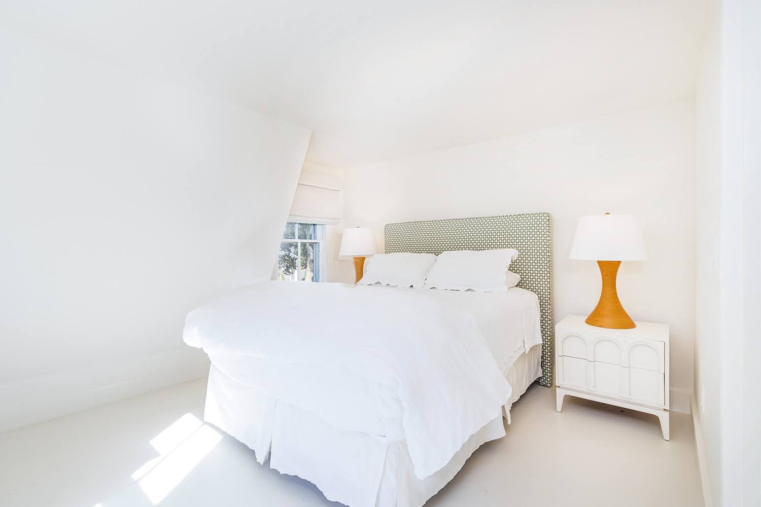 Serene white bedroom with patterned headboard, matching nightstands, and warm bedside lamps.