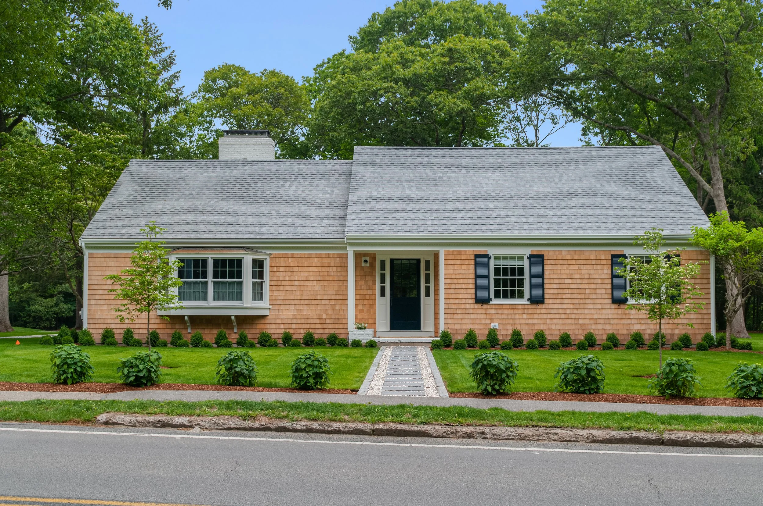 Shingled Cape Cod home with gray roof, black shutters, brick walkway, and custom coastal curb appeal.