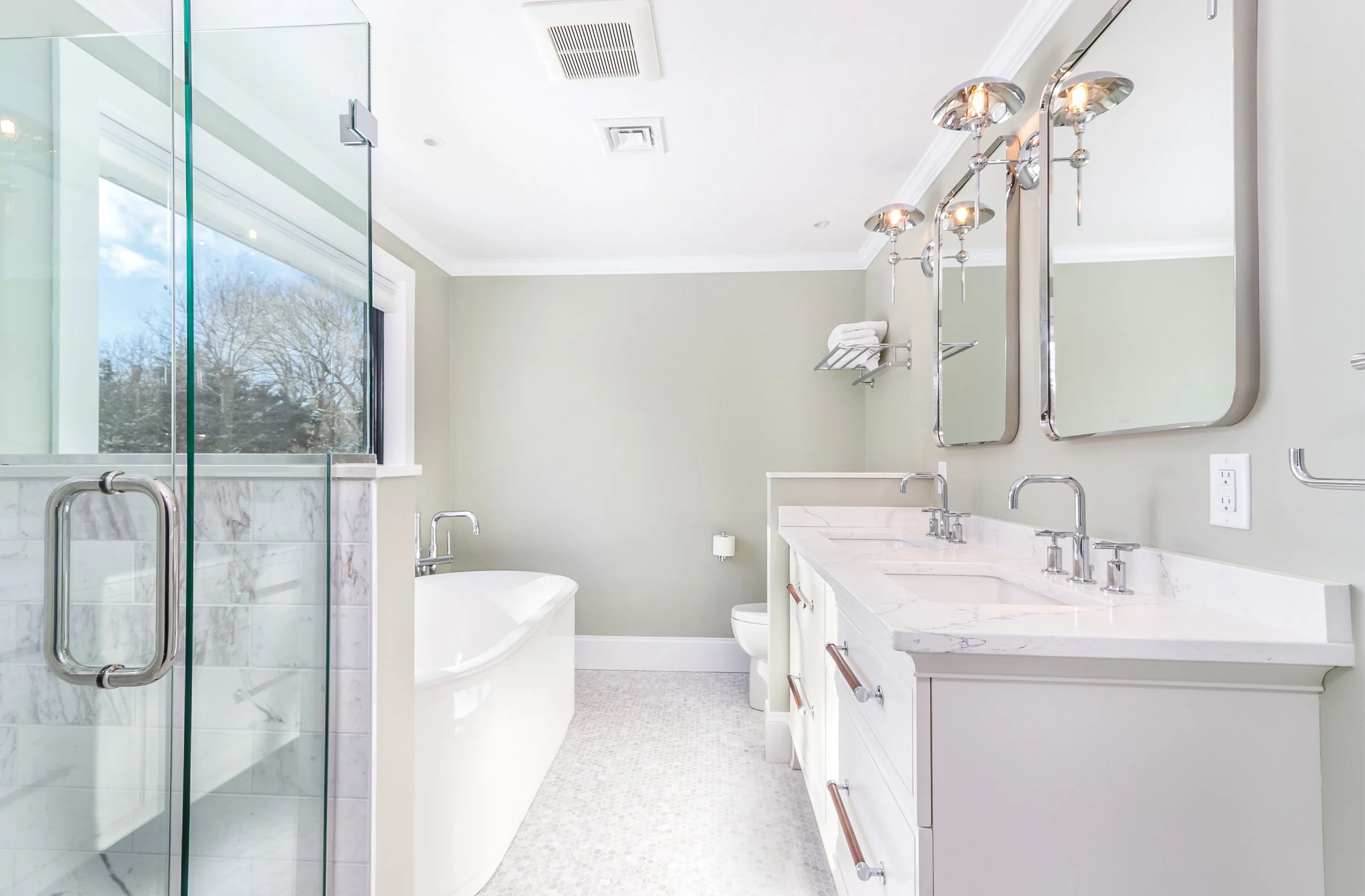 In this custom coastal home, a bright bath showcases a glass shower, freestanding tub, and marble-topped vanity.