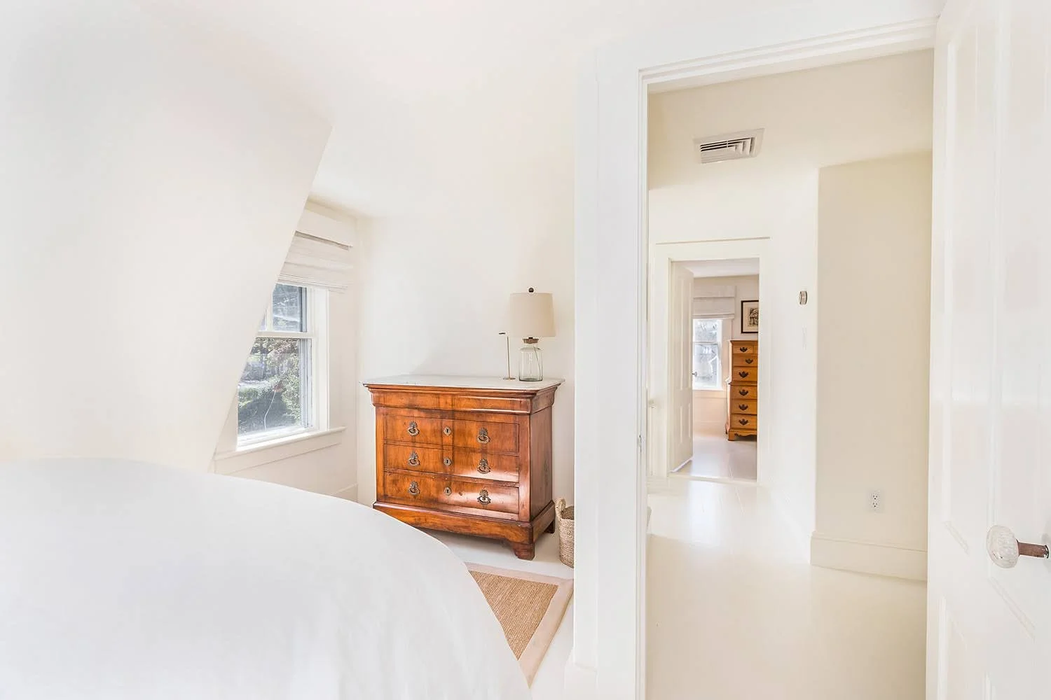 Angled ceiling, white walls, and antique wood dresser add character to this Cape Cod cottage bedroom.