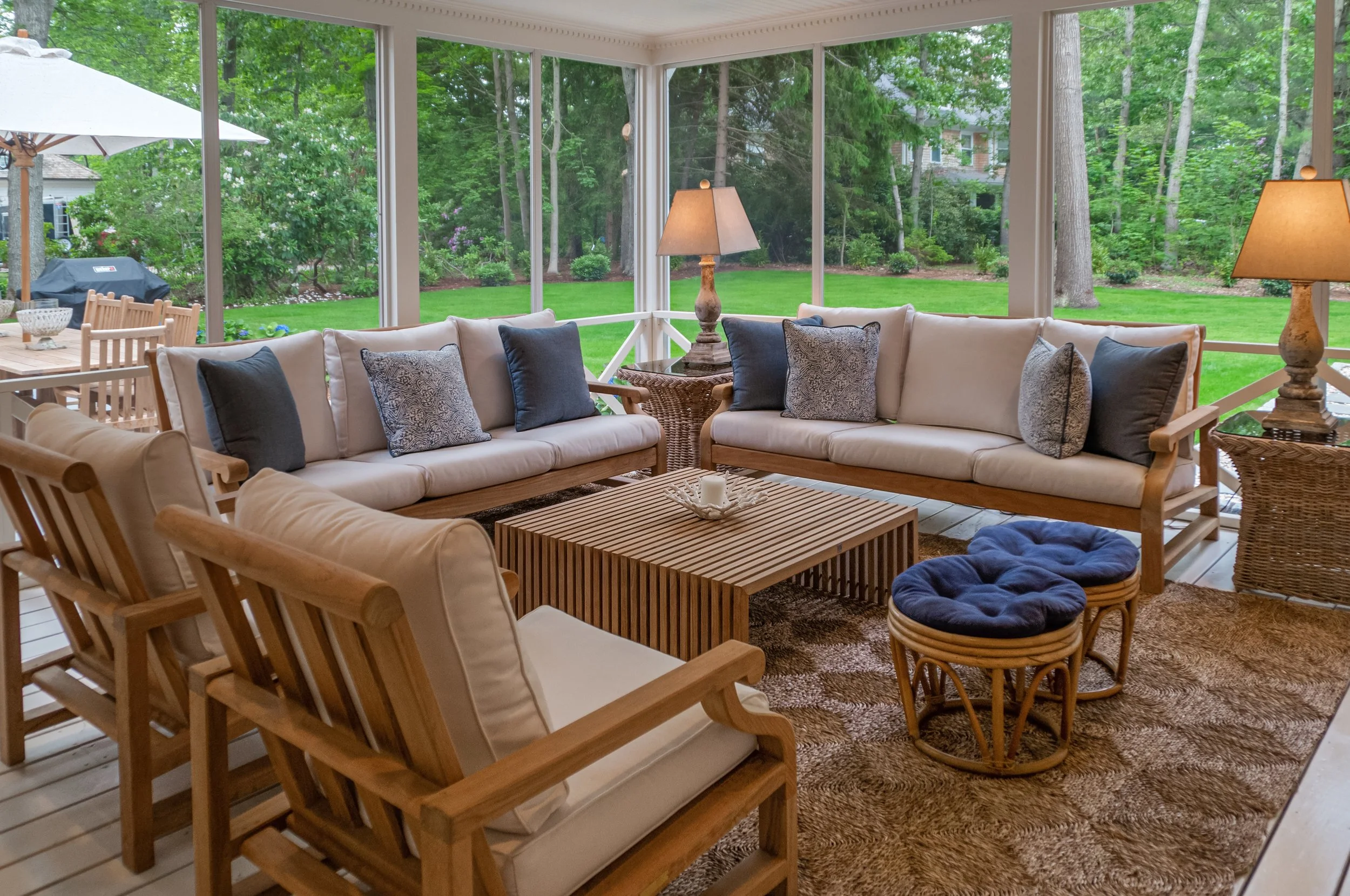 Screened porch in a custom Cape Cod home with cushioned seating, woven accents, and wooded backyard views.