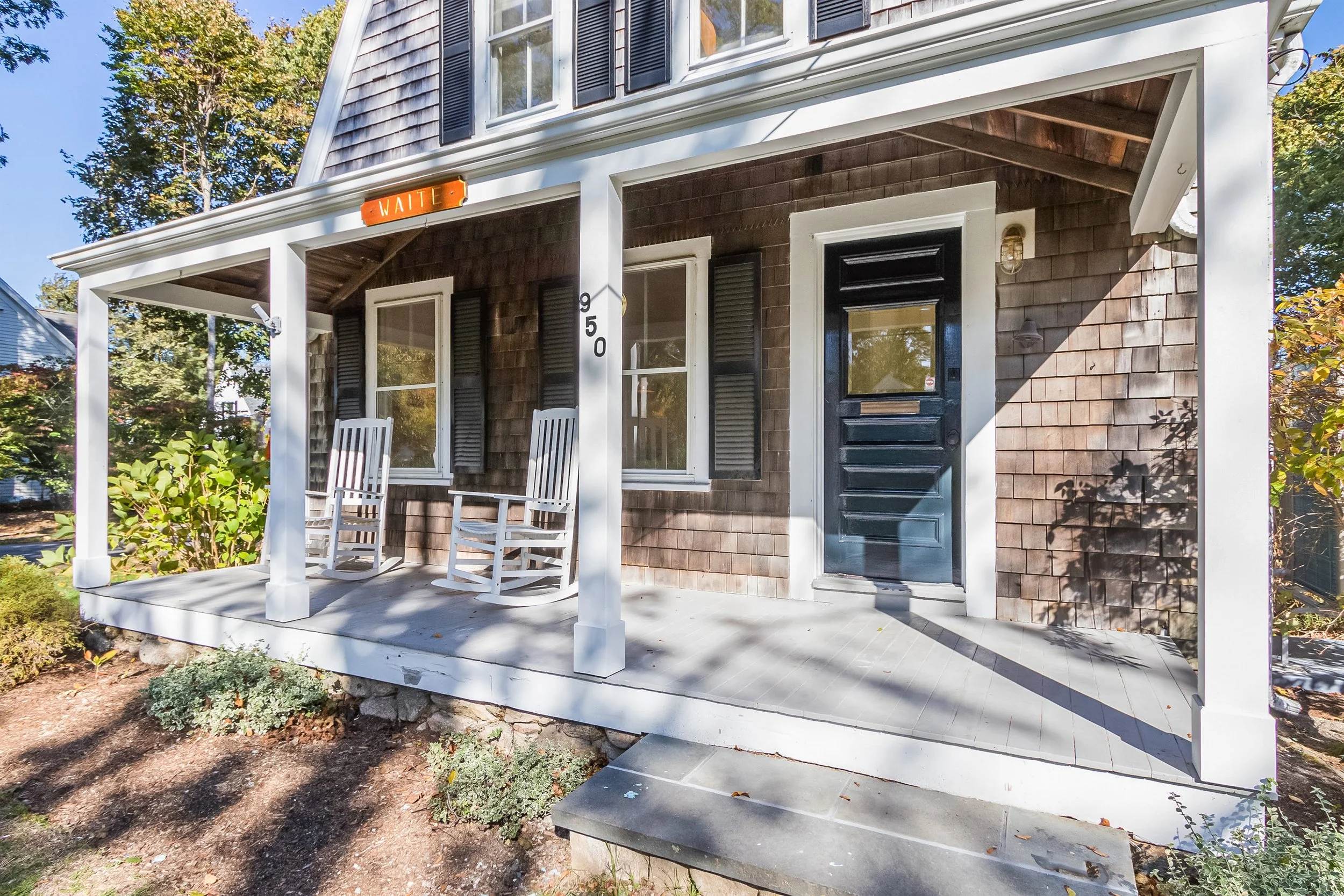 Front porch with rocking chairs, black shutters, and weathered shingles for Cape Cod cottage renovation appeal.