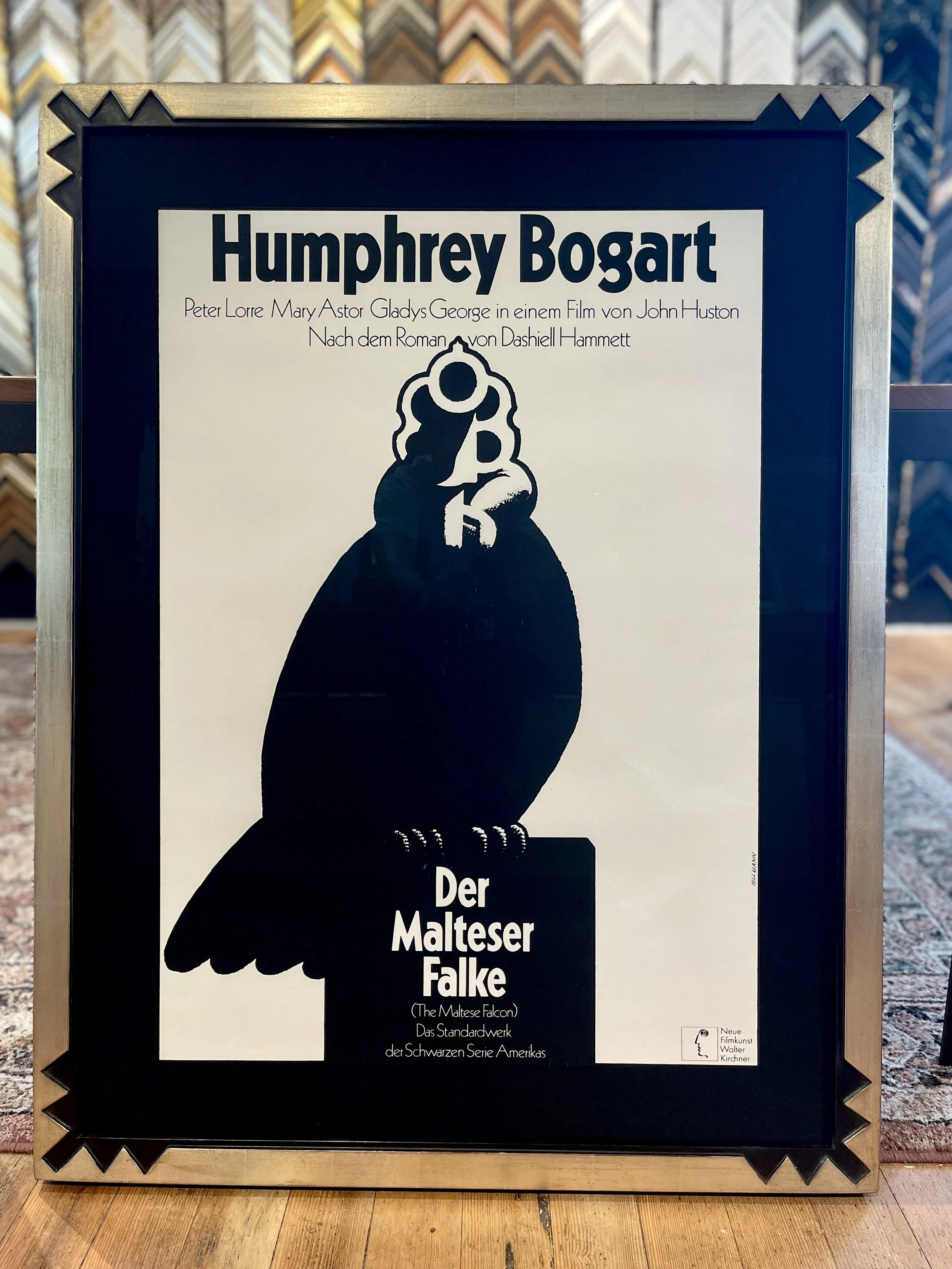 A framed movie poster for 'Der Maltese Falke' featuring a black silhouette of a Maltese falcon bird.