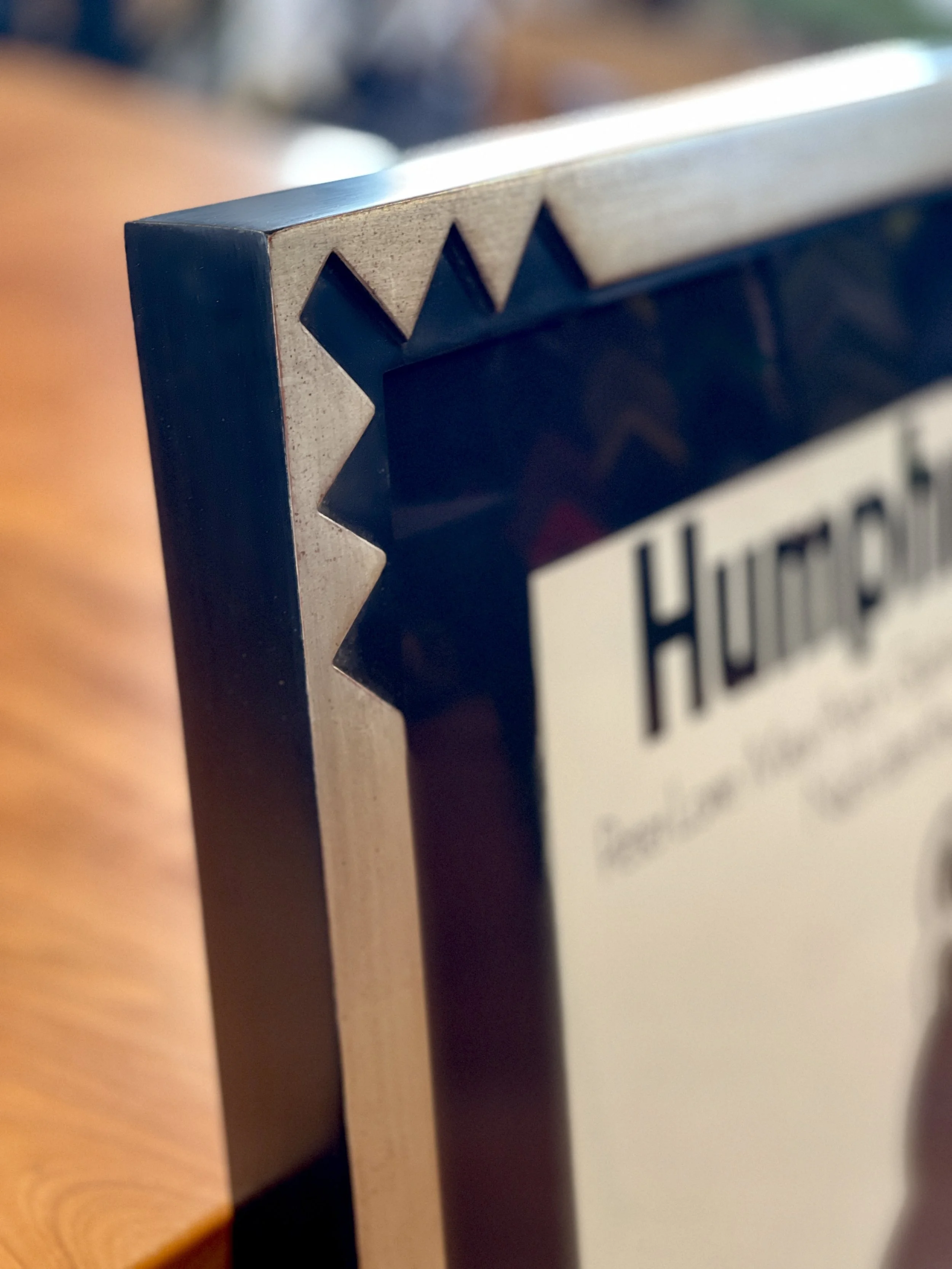 Close-up of a decorative black and natural wood framed sign with a star design in the corner, partially visible text reading 'HURC' and some blurry text below.