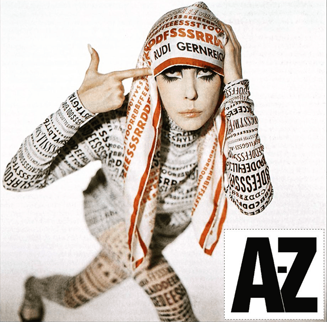 Model wearing clothing with letters all over it. She has dramatic eyeliner, and pointing to her head.