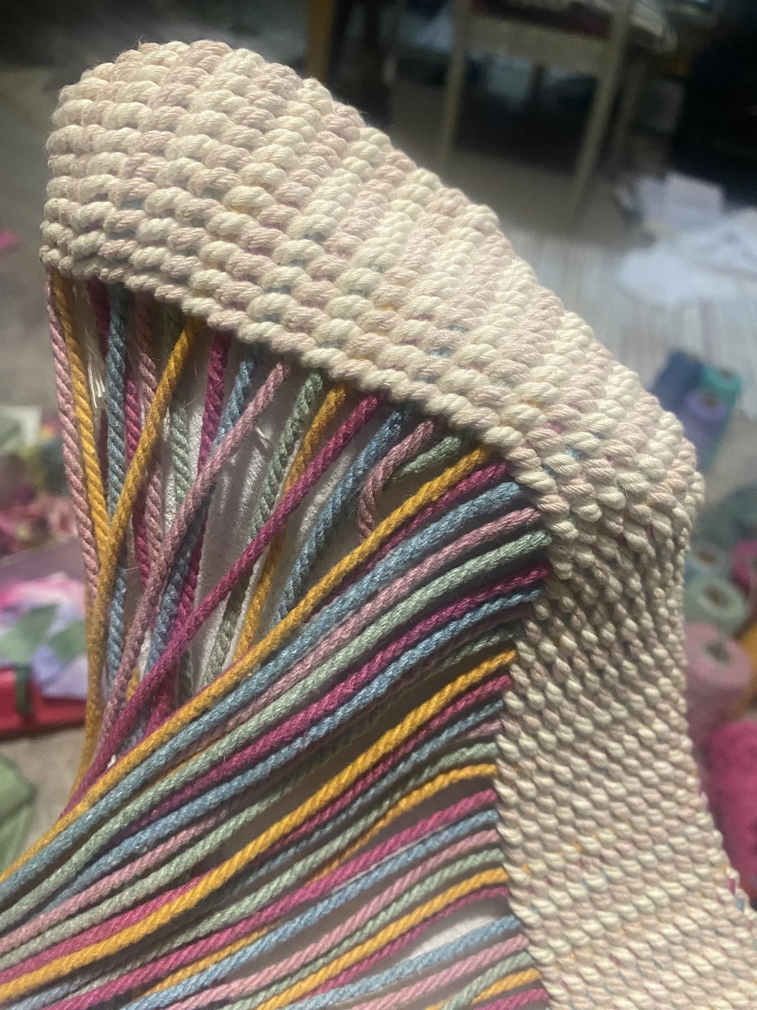 Work in progress, close-up of weaving over an object with pastel-colored warp threads.