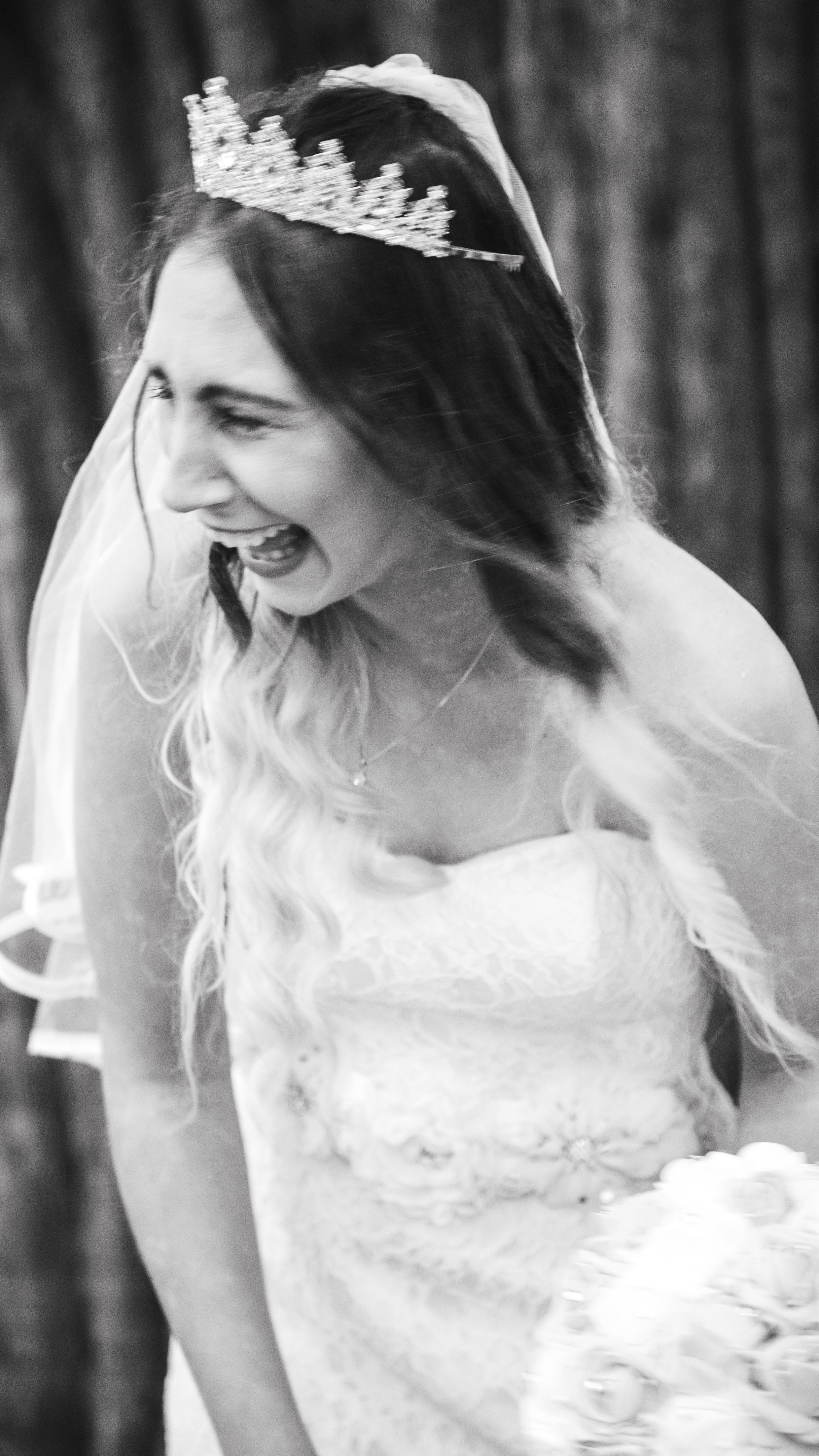 Bride laughing with a tiara and bouquet, wearing a lace wedding dress.