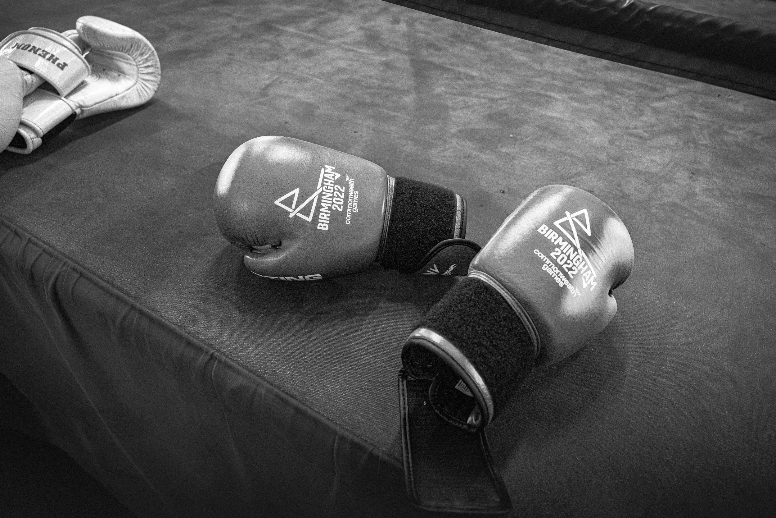Pair of boxing gloves on a padded surface with another pair partially visible in the background