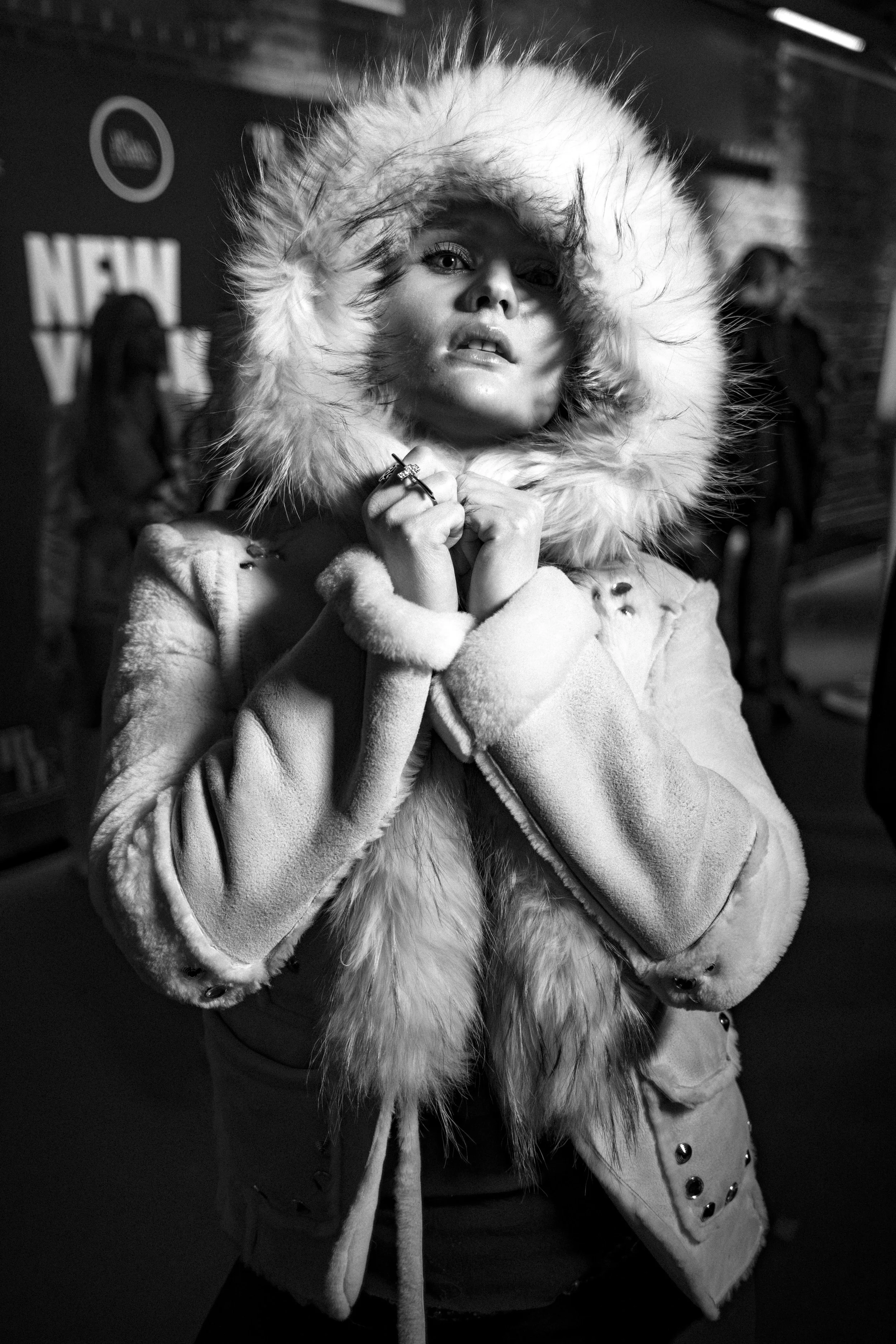 A woman in a fur-lined winter coat with her hood up, looking at the camera, in a black and white photo.