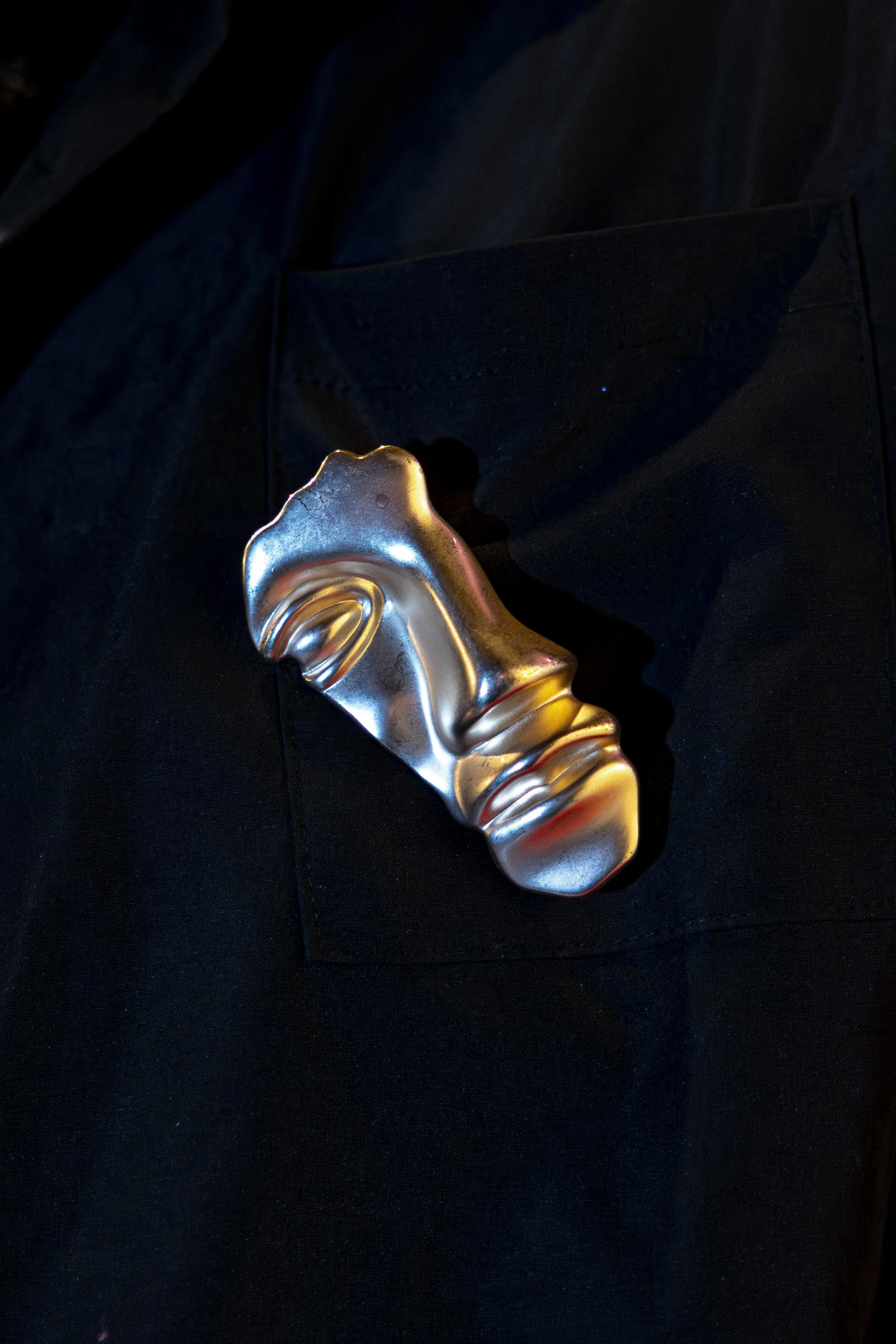A metallic mask with a gold and silver finish lying on black fabric.