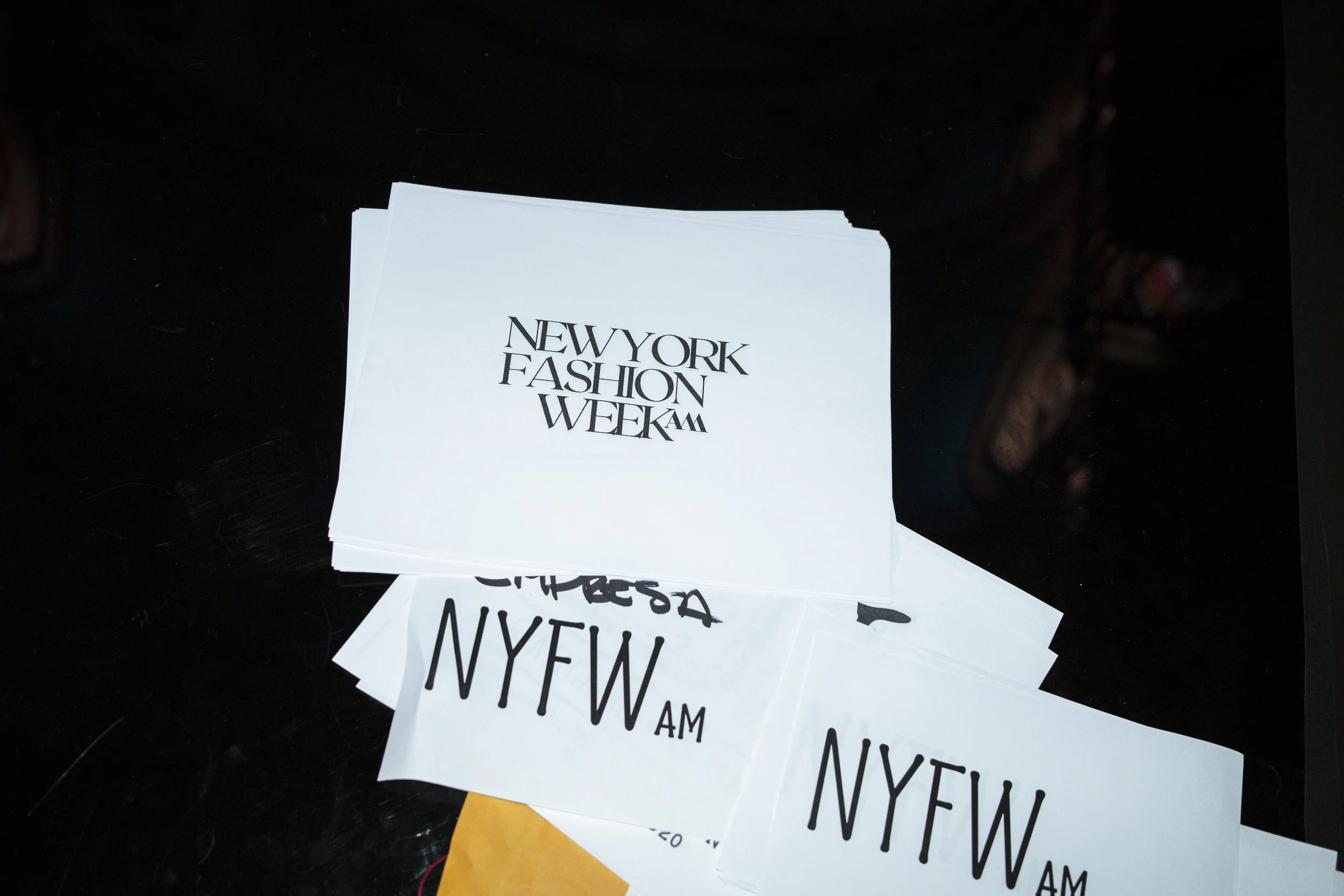 A stack of paper cards or flyers with the text 'NEW YORK FASHION WEEK AM' visible on the top card.