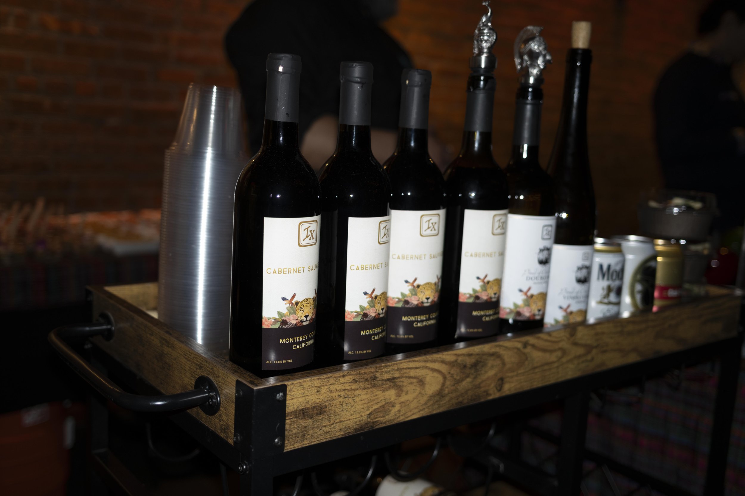 Several bottles of Cabernet Sauvignon wine from Monterey County, California, with labels featuring a lion illustration, placed on a wooden bar counter.