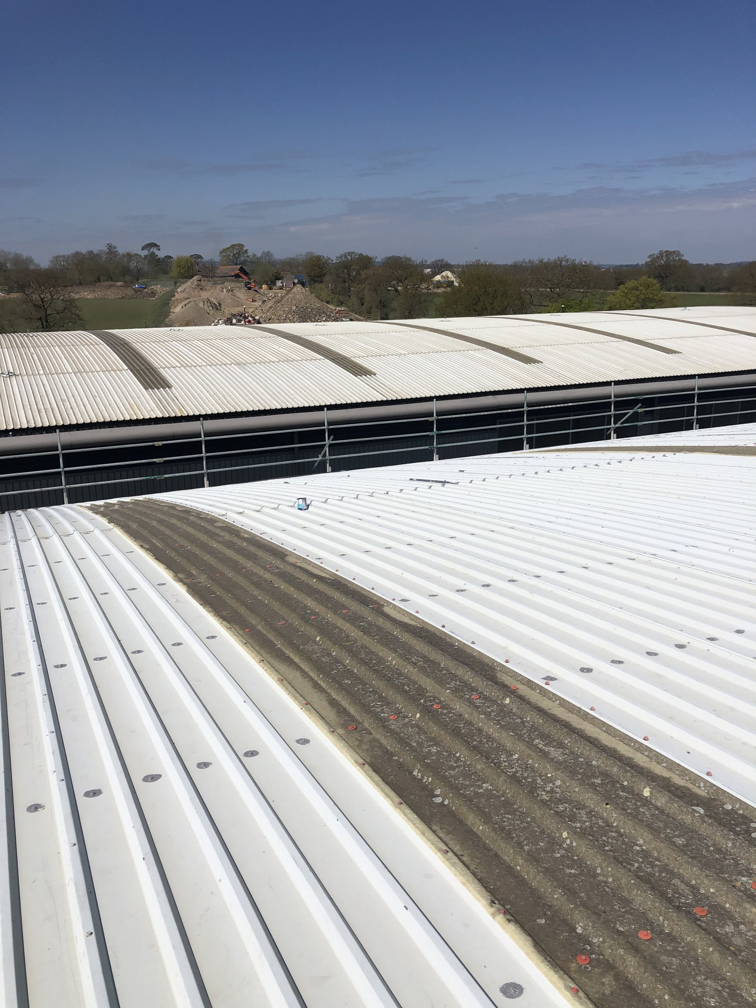 View of two white corrugated metal roofs with a clear blue sky in the background and construction materials in the distance.