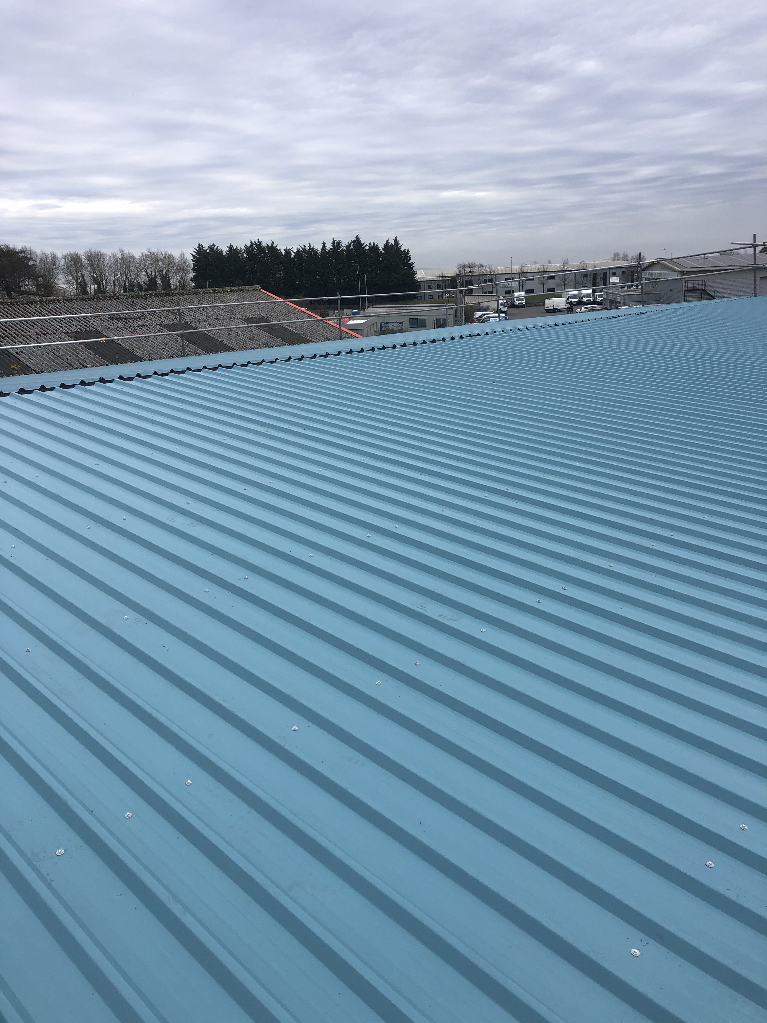 Blue corrugated metal roof with industrial area in the background under cloudy sky.