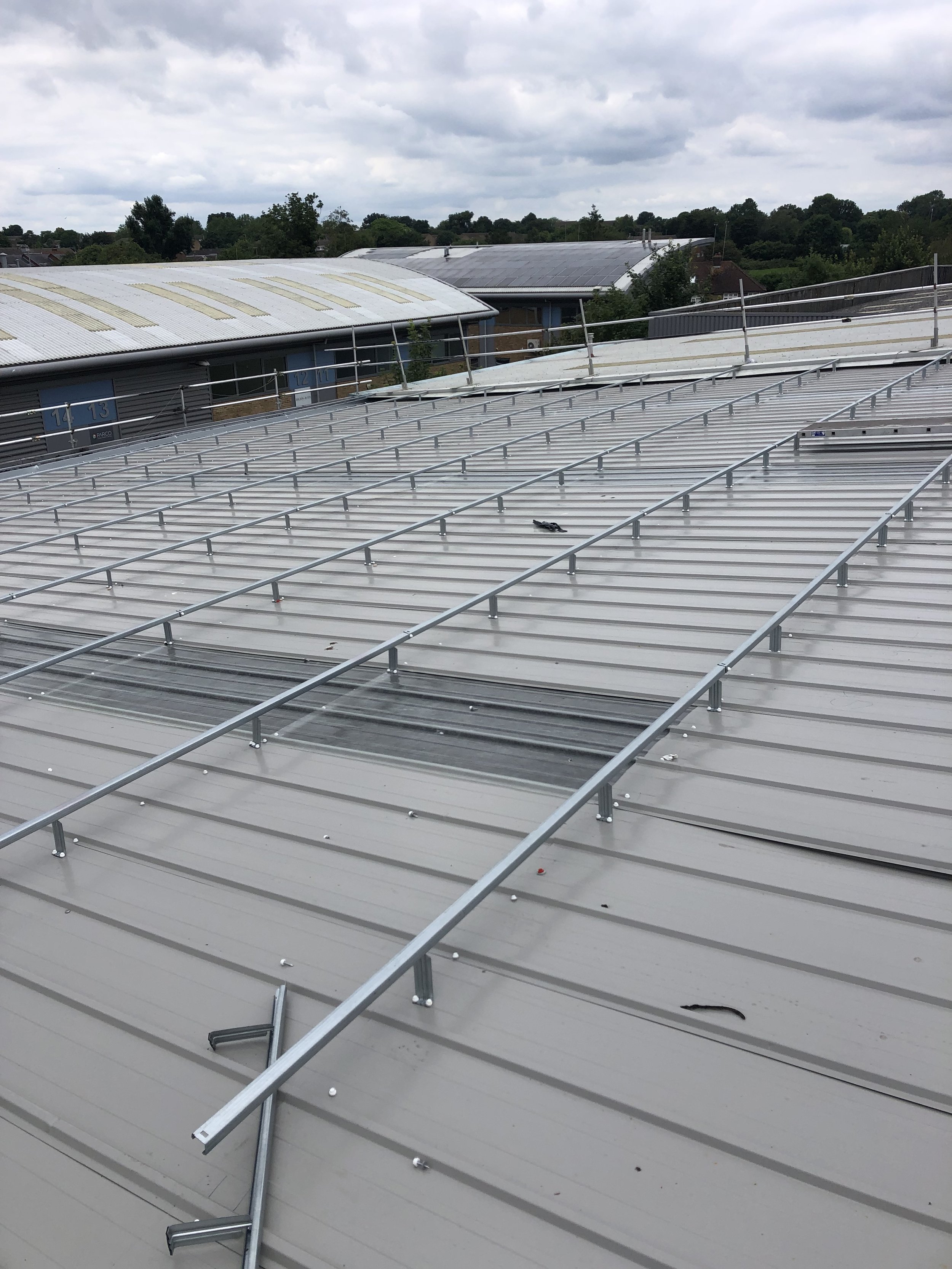 Metal roof with mounting rails for solar panels, overcast sky, and distant trees