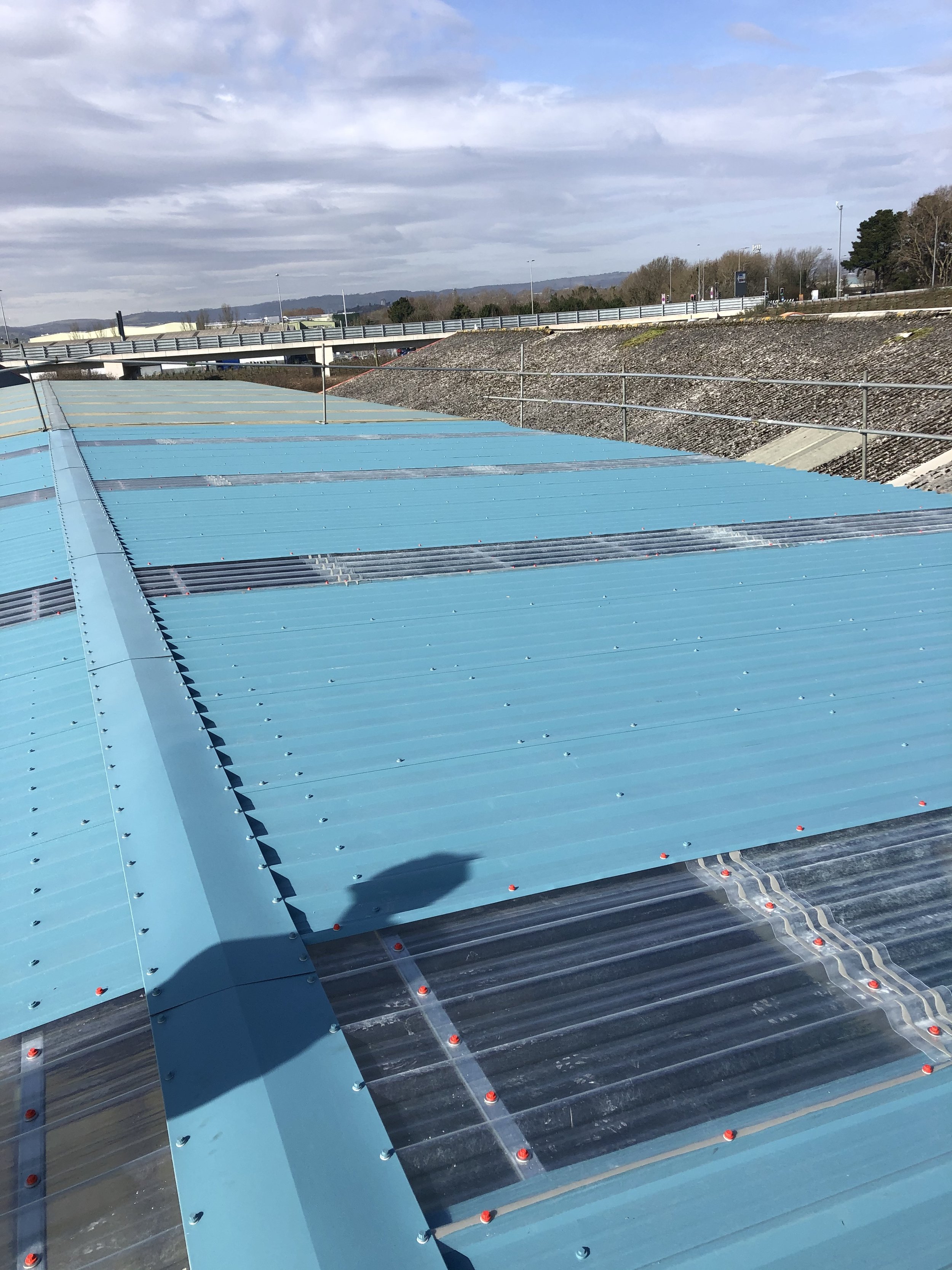 Blue metal rooftop with skylights, set against a cloudy sky and distant highway.